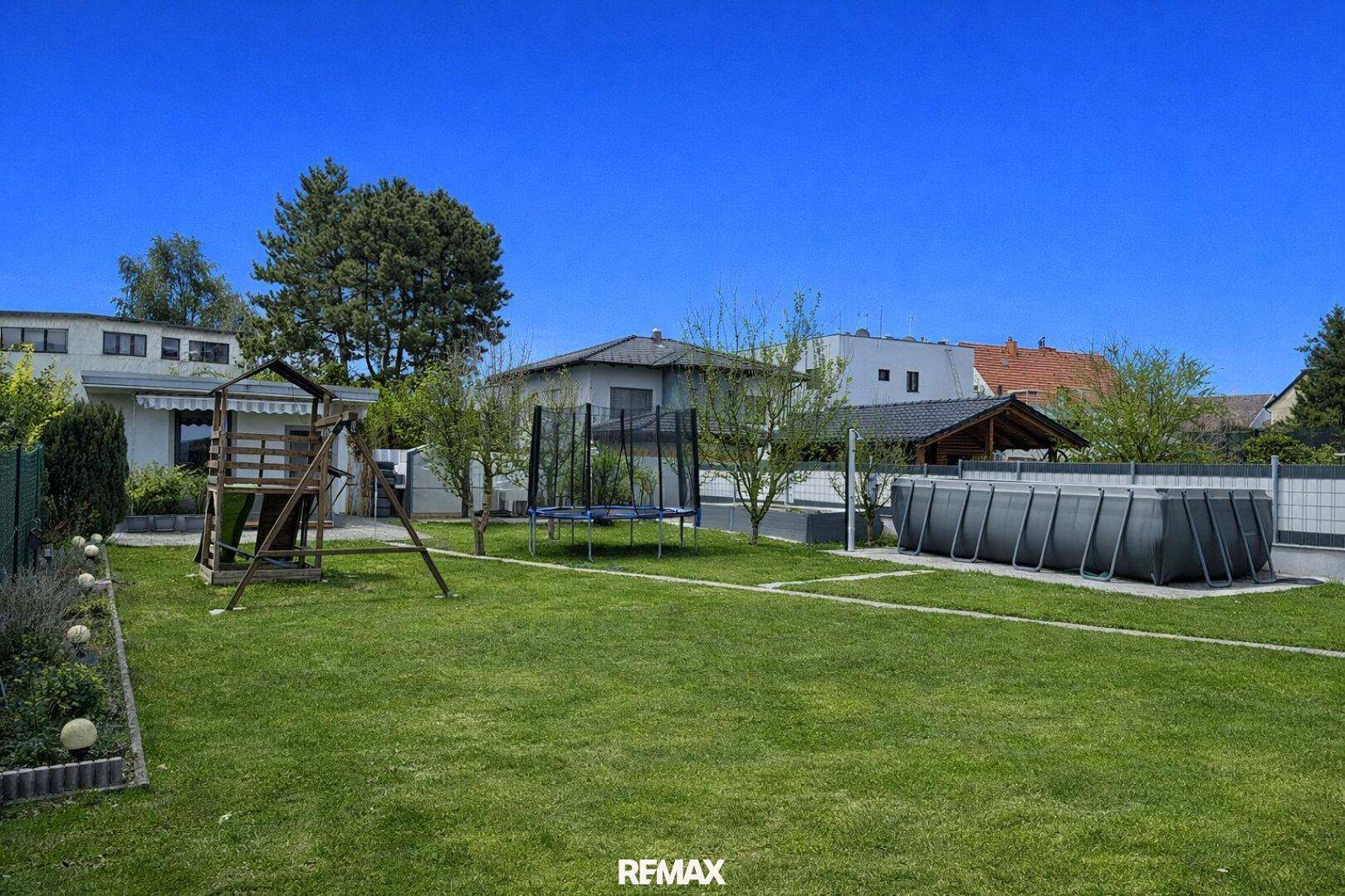 Großer, gepflegter Garten mit Rasenfläche, Trampolin, Spielplatz und Aufstellpool.