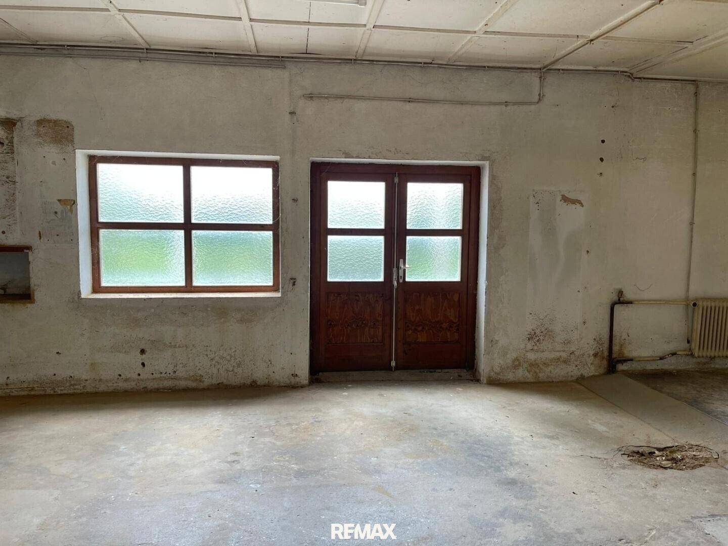 Innenansicht eines Lagerraums mit Betonboden, Fenster und Heizkörper, der Renovierung benötigt.