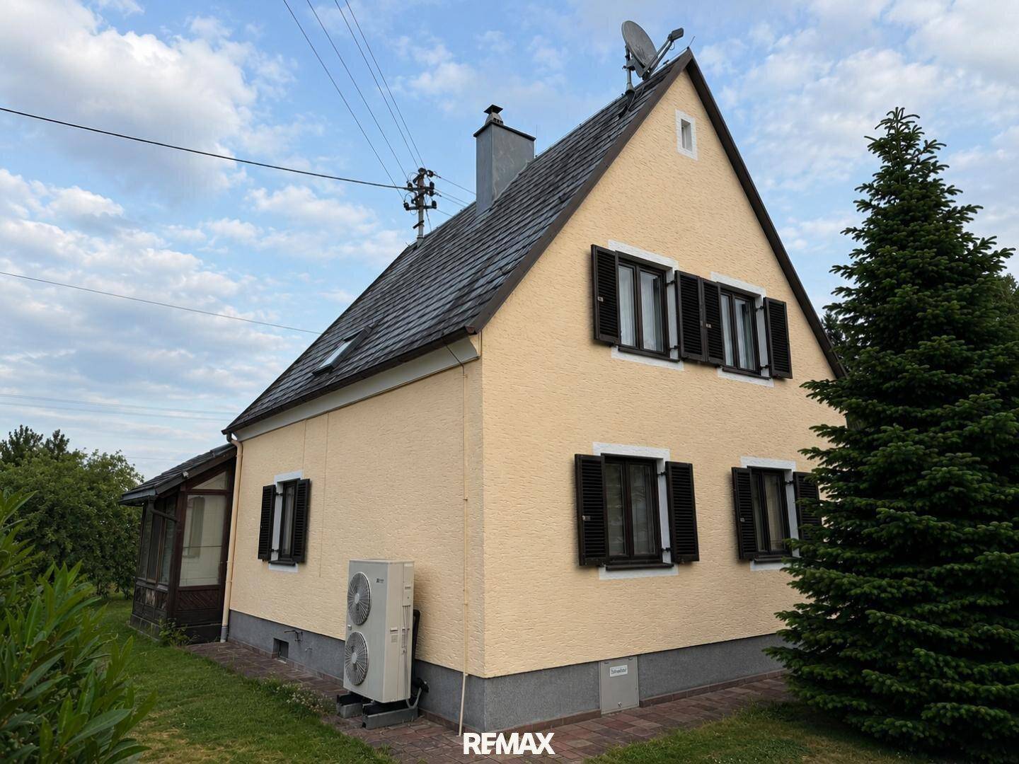 Seitenansicht des Hauses mit gelber Fassade, Satteldach und sichtbarer Klimaanlage im Außenbereich.