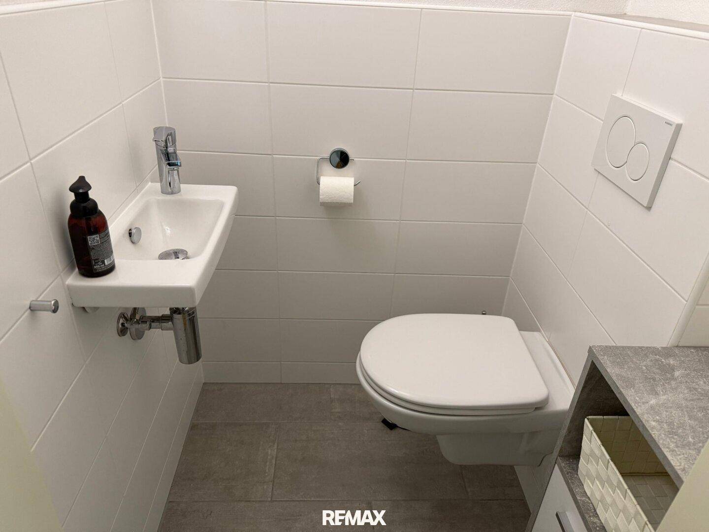 Kleines Gäste-WC mit wandhängender Toilette und Handwaschbecken, weiß gefliest.
