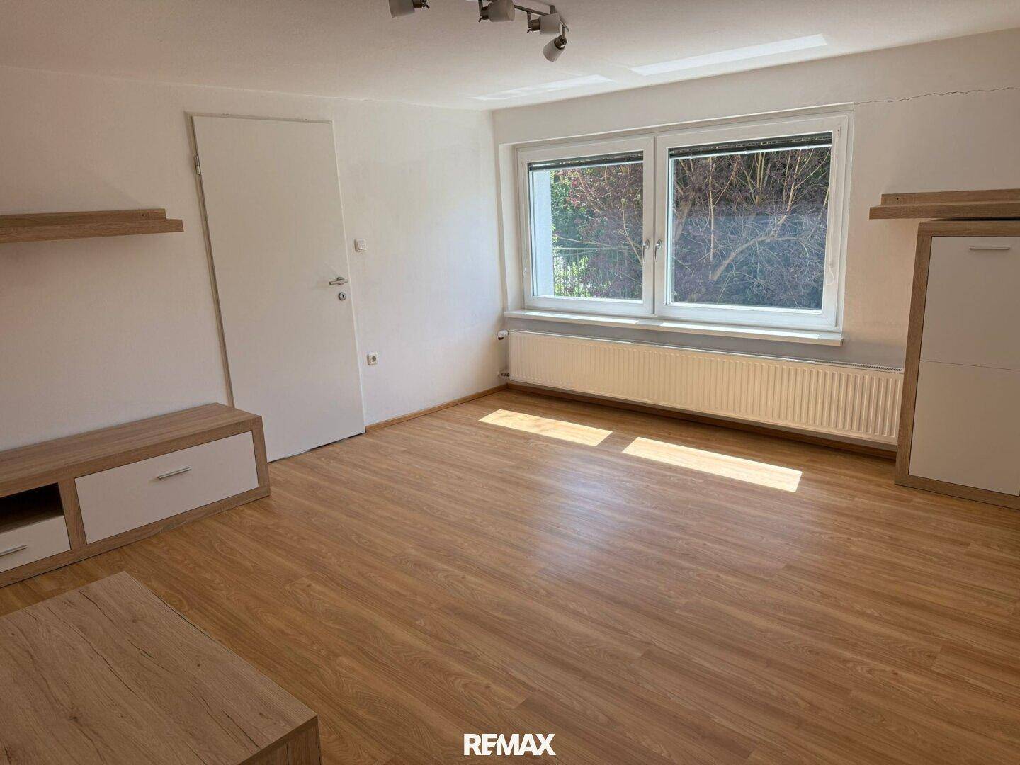 Geräumiger Raum mit großem Fenster, Laminatboden und viel Tageslicht.