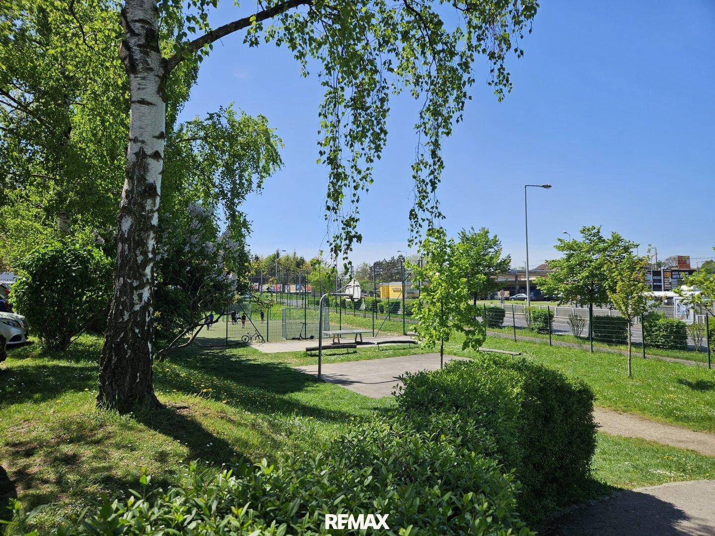 Grüner Außenbereich mit Bäumen und einem kleinen Spielplatz, ideal für Familien.