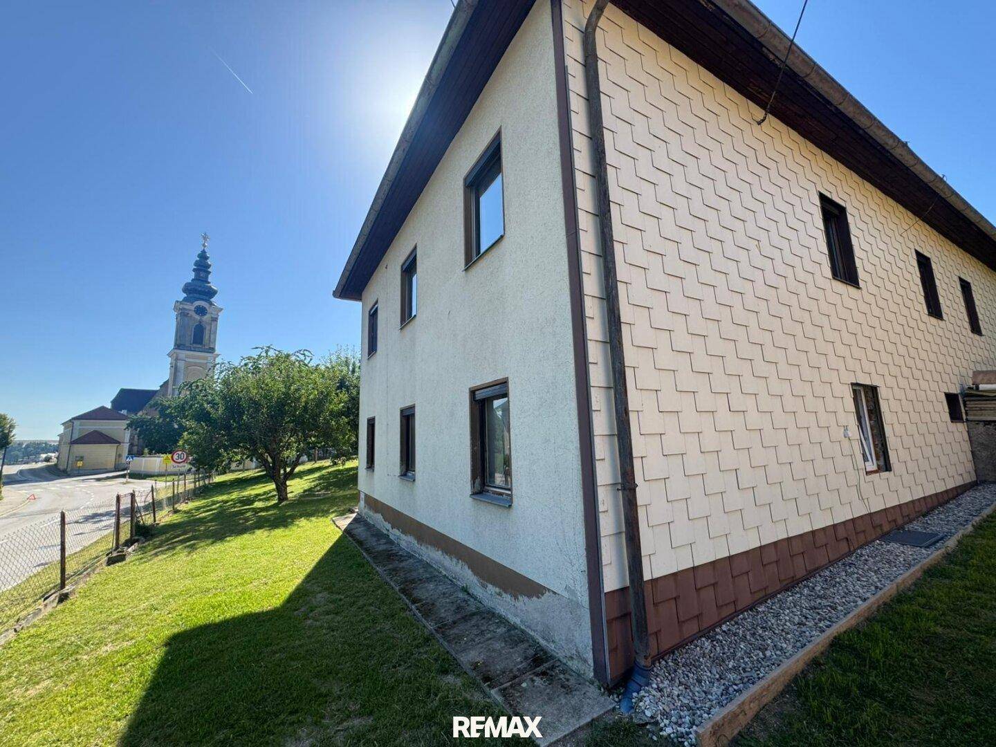 Fassade des Hauses mit dekorativen Schindeln und Blick auf die Kirchturmspitze.