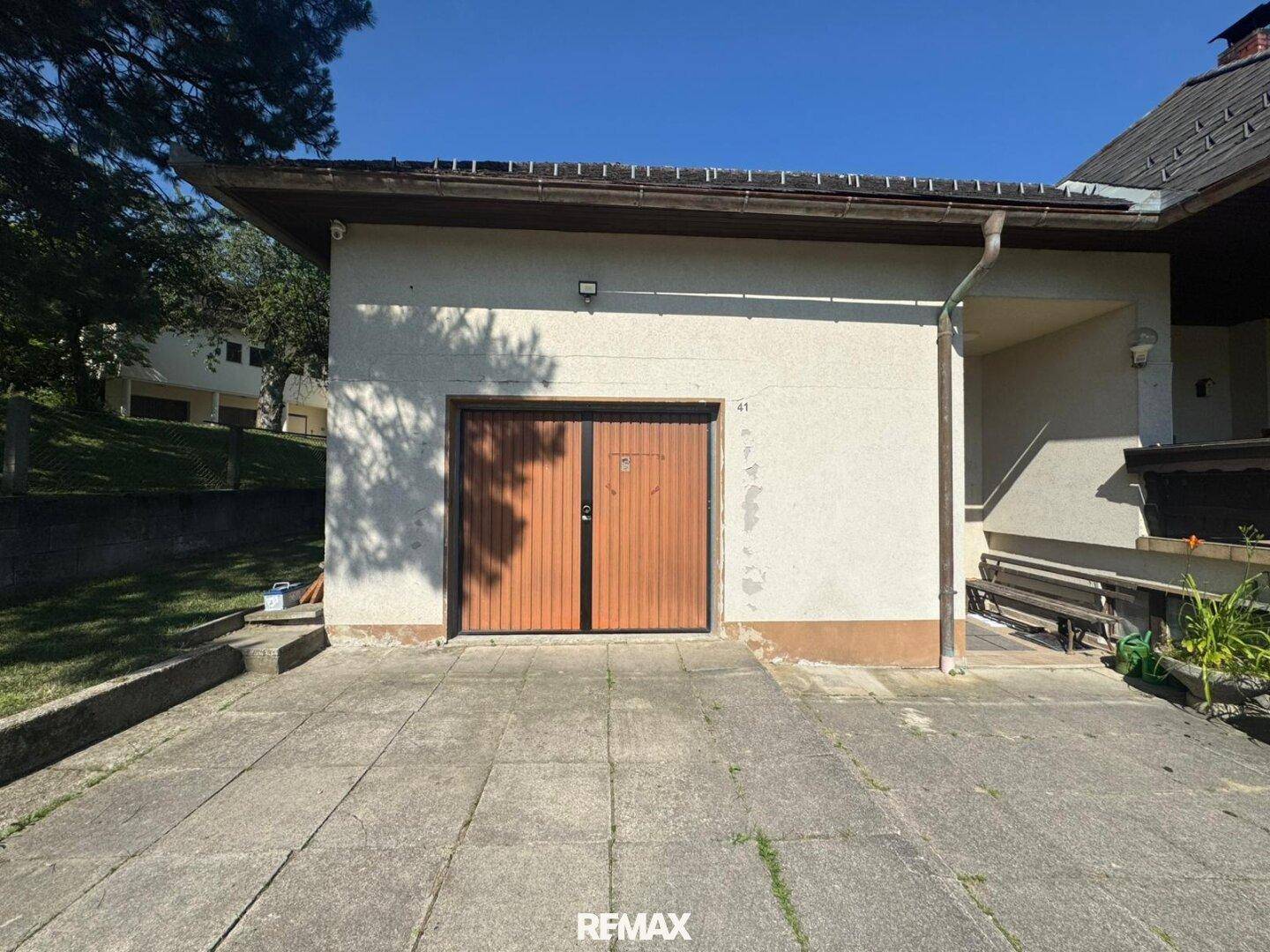 Einfahrt zur Garage mit Holztoren und gepflastertem Vorplatz.