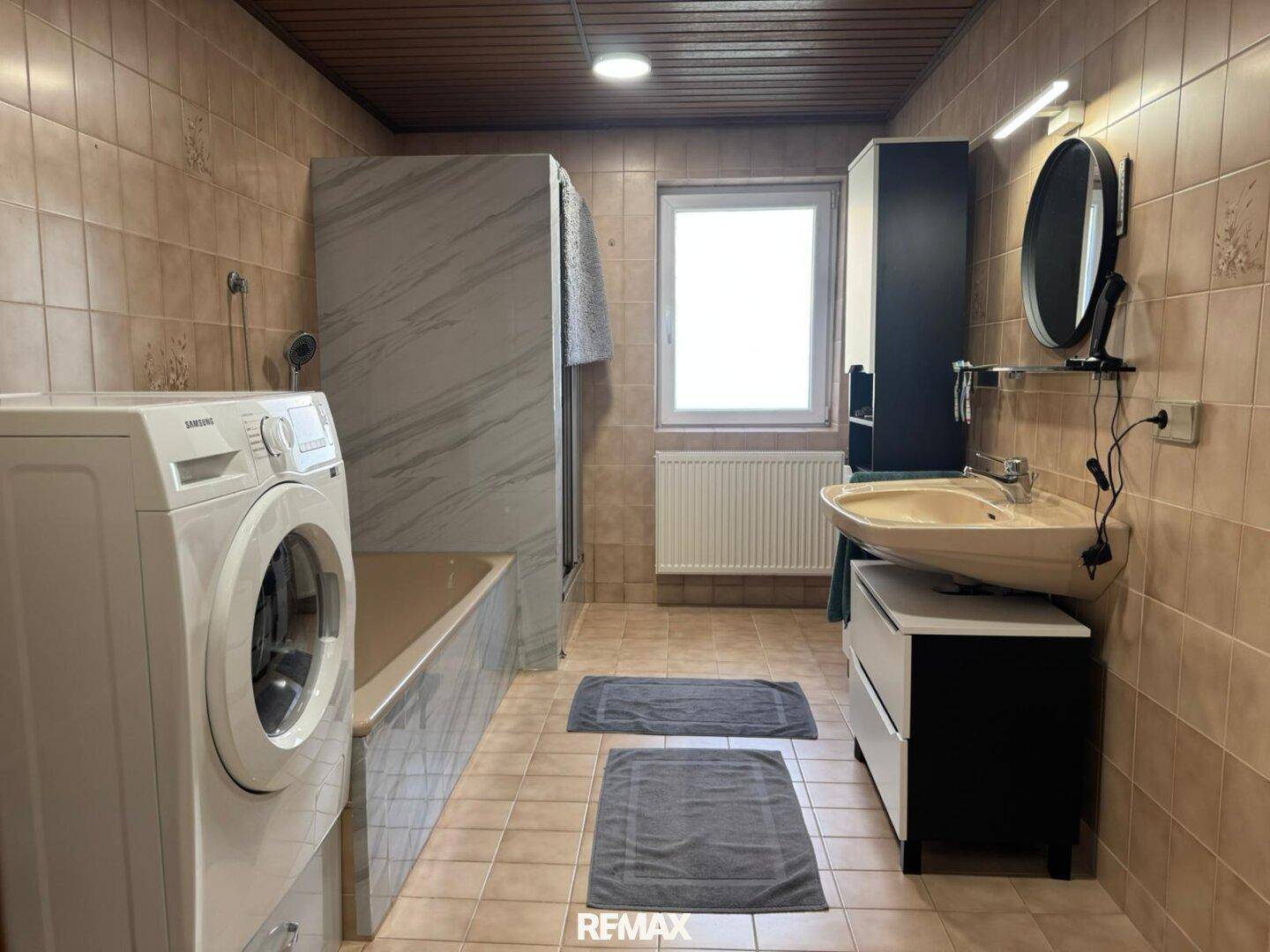 Gefliestes Badezimmer mit Badewanne, Dusche, Waschbecken und Waschmaschine.