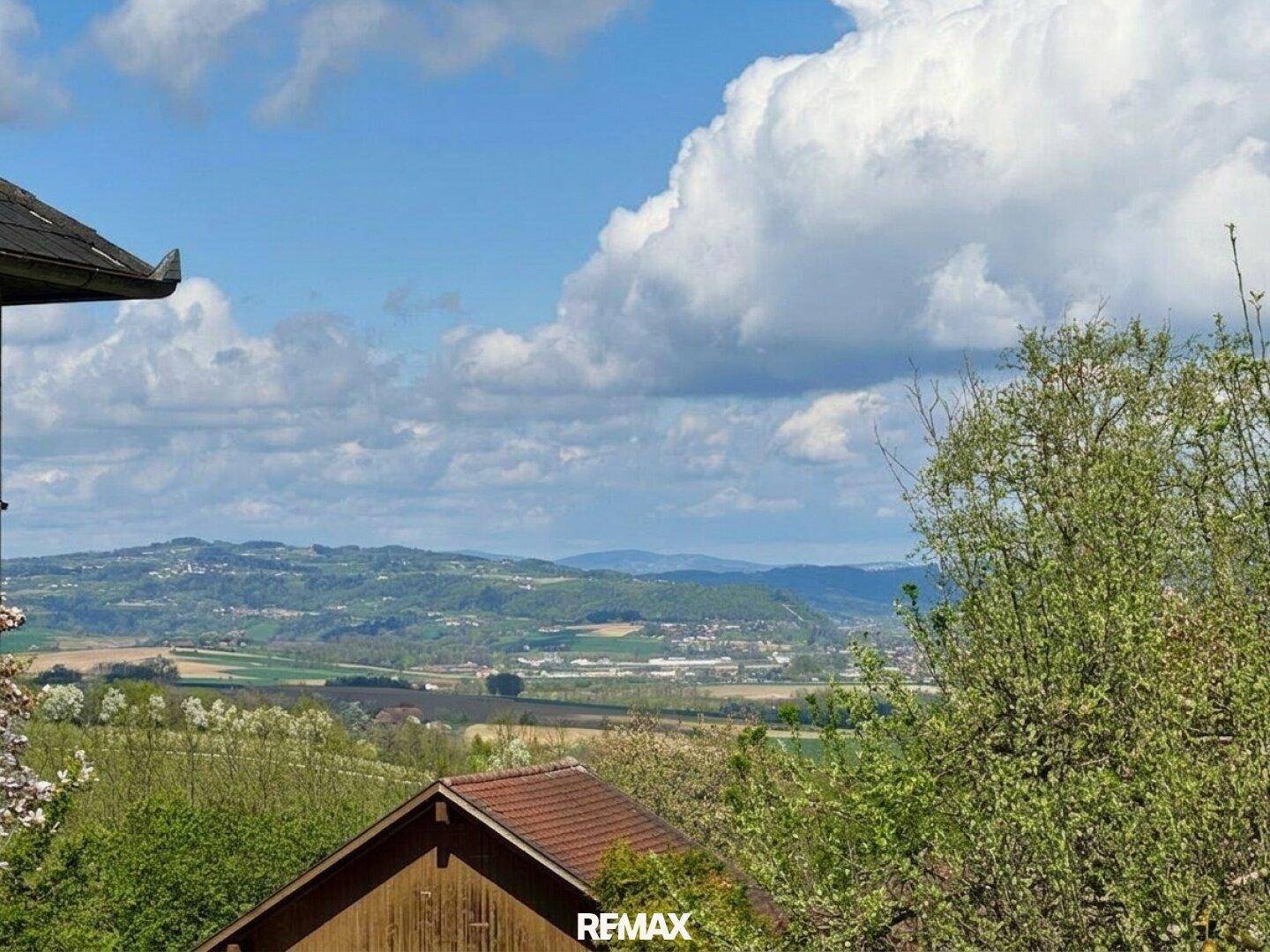 Weitläufiger Blick über die grüne Landschaft und Hügel unter bewölktem Himmel.