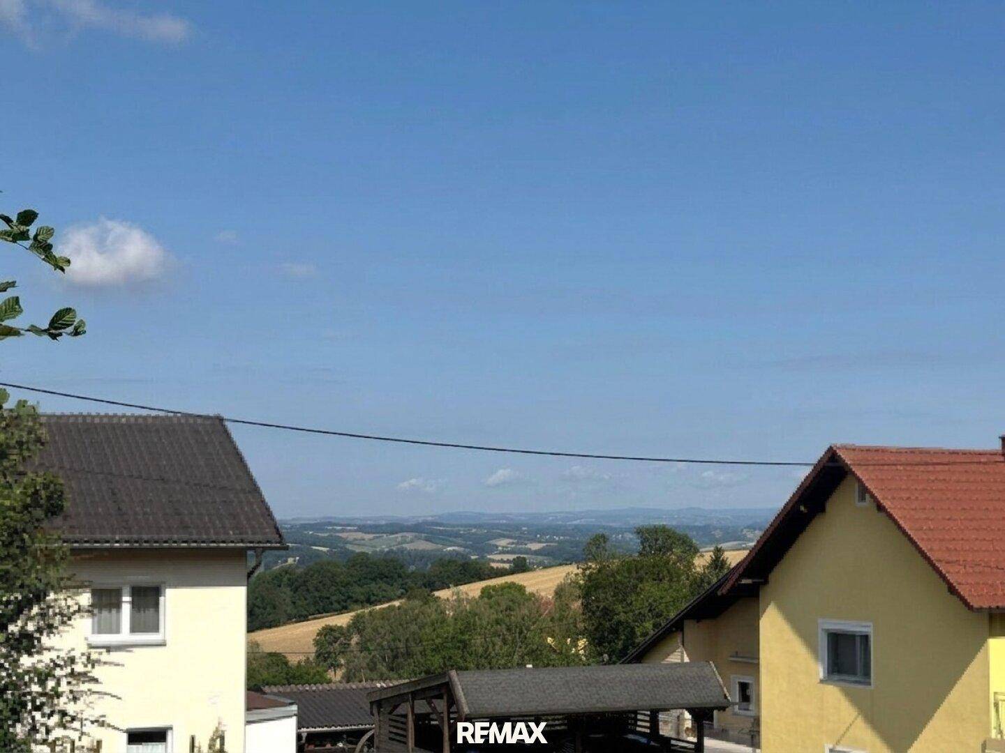 Panoramablick über die hügelige Landschaft mit Feldern und vereinzelten Häusern unter klarem Himmel.
