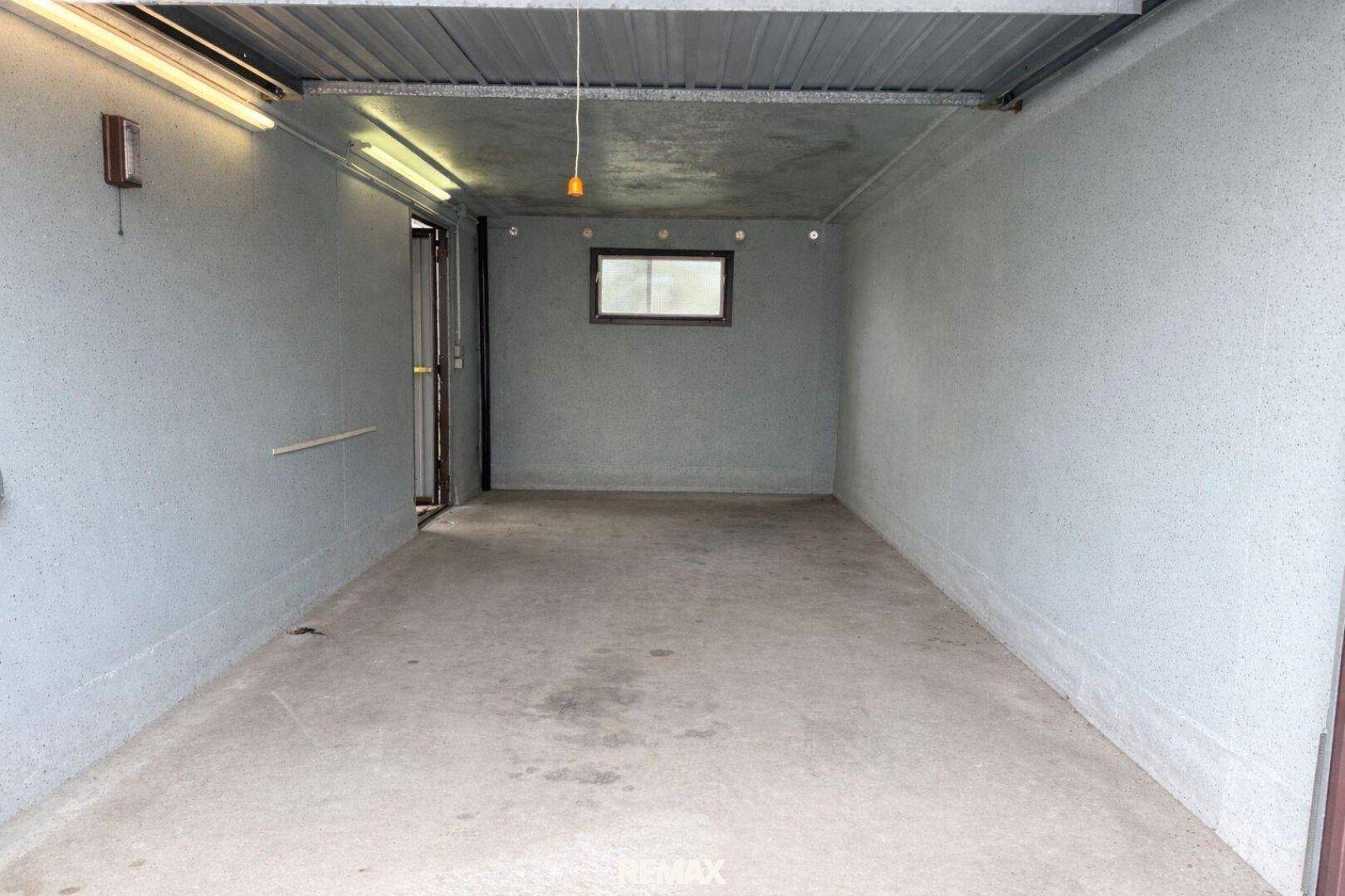 Geräumige Garage mit Betonboden und einem kleinen Fenster für Belüftung und Tageslicht.