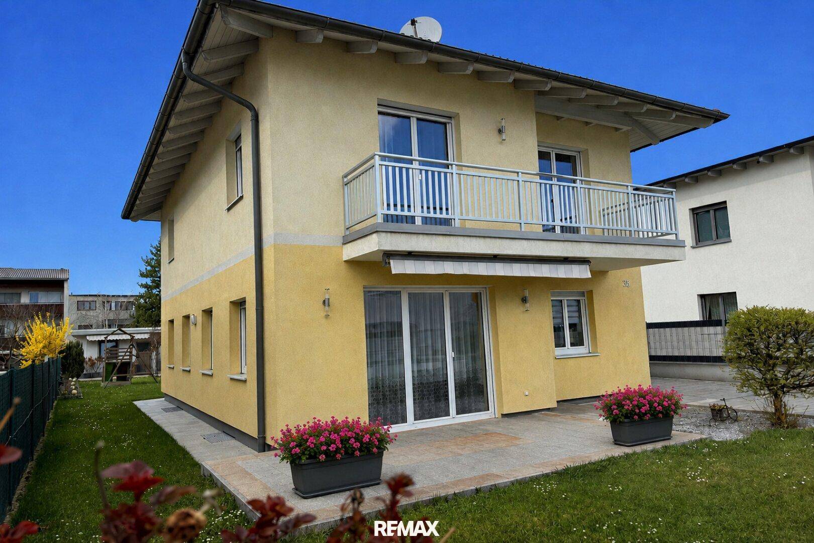 Seitenansicht des gelben Hauses mit kleiner Terrasse und gepflegtem Rasenbereich.