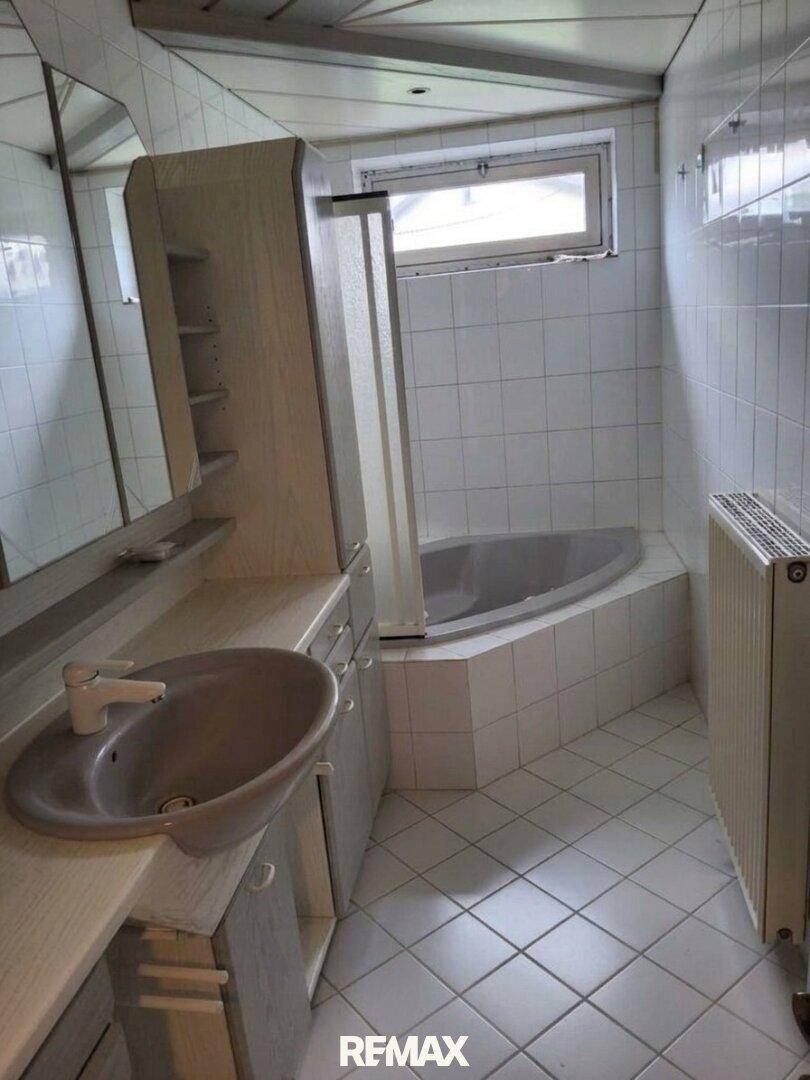 Badezimmer mit Eckbadewanne, Waschbecken und Fenster.