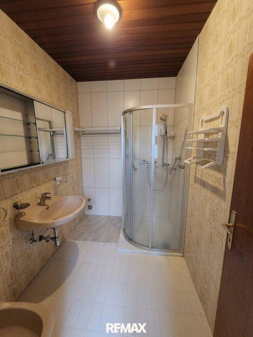 Badezimmer mit Duschkabine, Waschbecken und gefliesten Wänden.