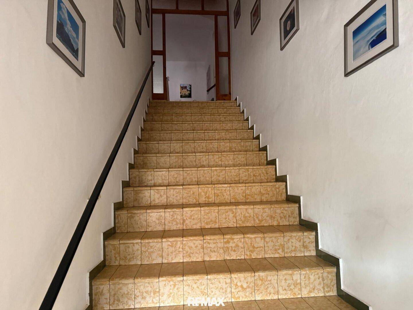 Geflieste Treppe mit Holzgeländer führt in die oberen Stockwerke.