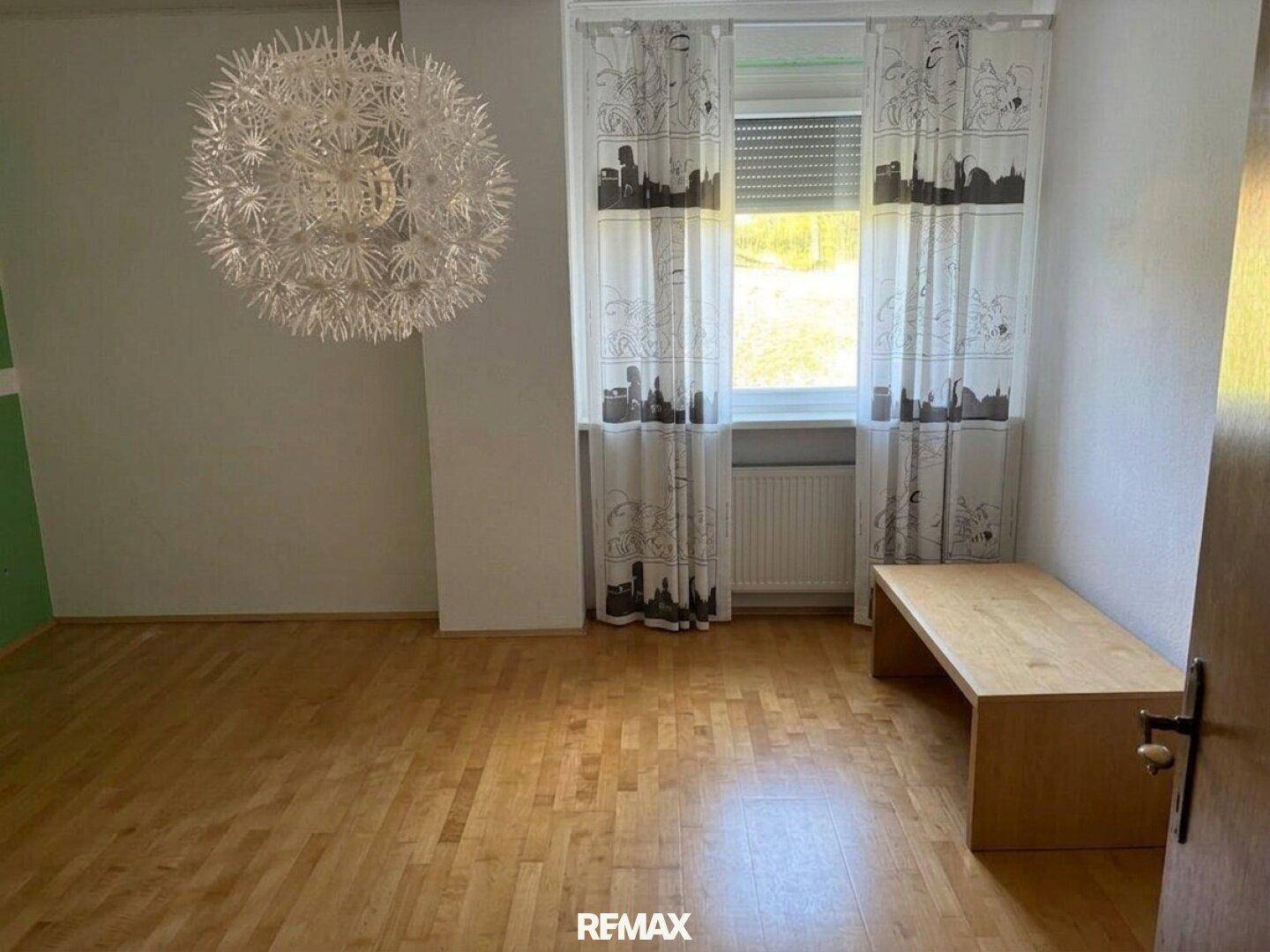 Helles Schlafzimmer mit Holzboden, Fenster und dekorativer Deckenleuchte.