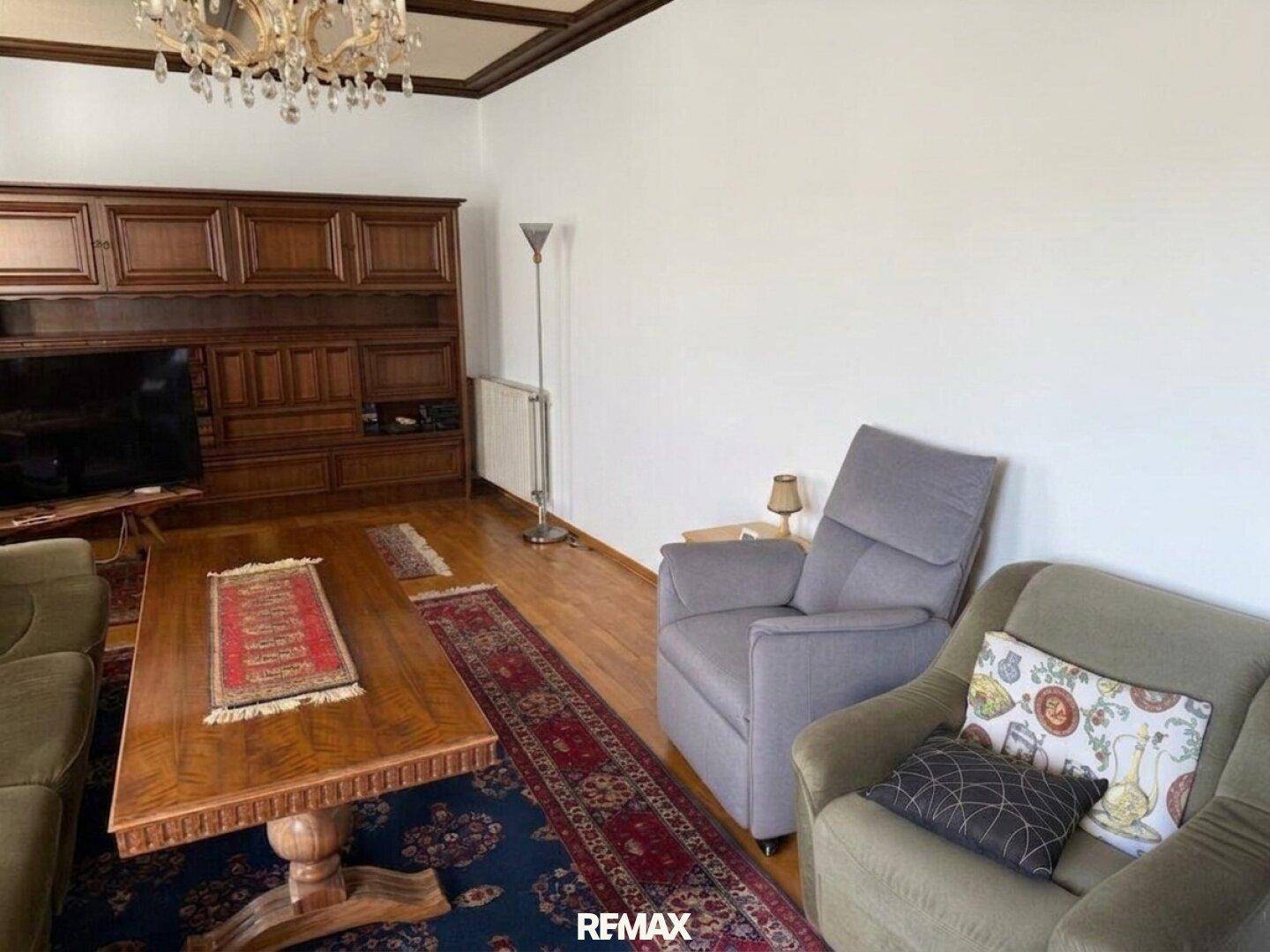 Geräumiges Wohnzimmer mit Holzboden, großem Schrank und bequemen Sesseln.