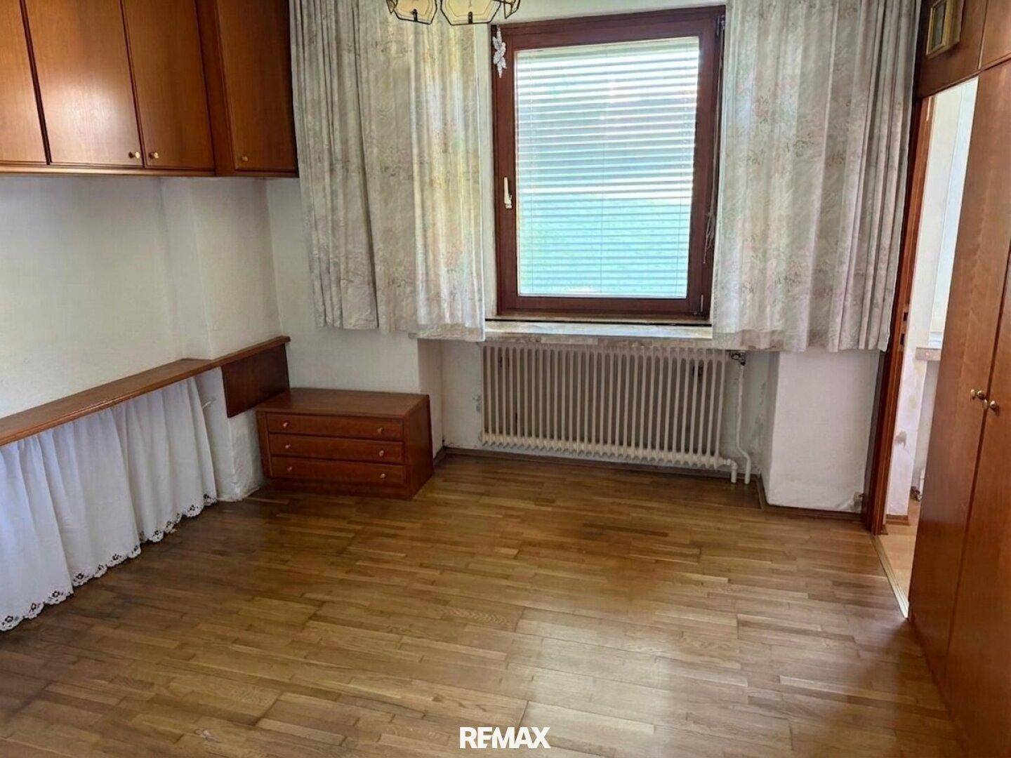 Schlafzimmer mit Holzboden, Fenster und Heizkörper.