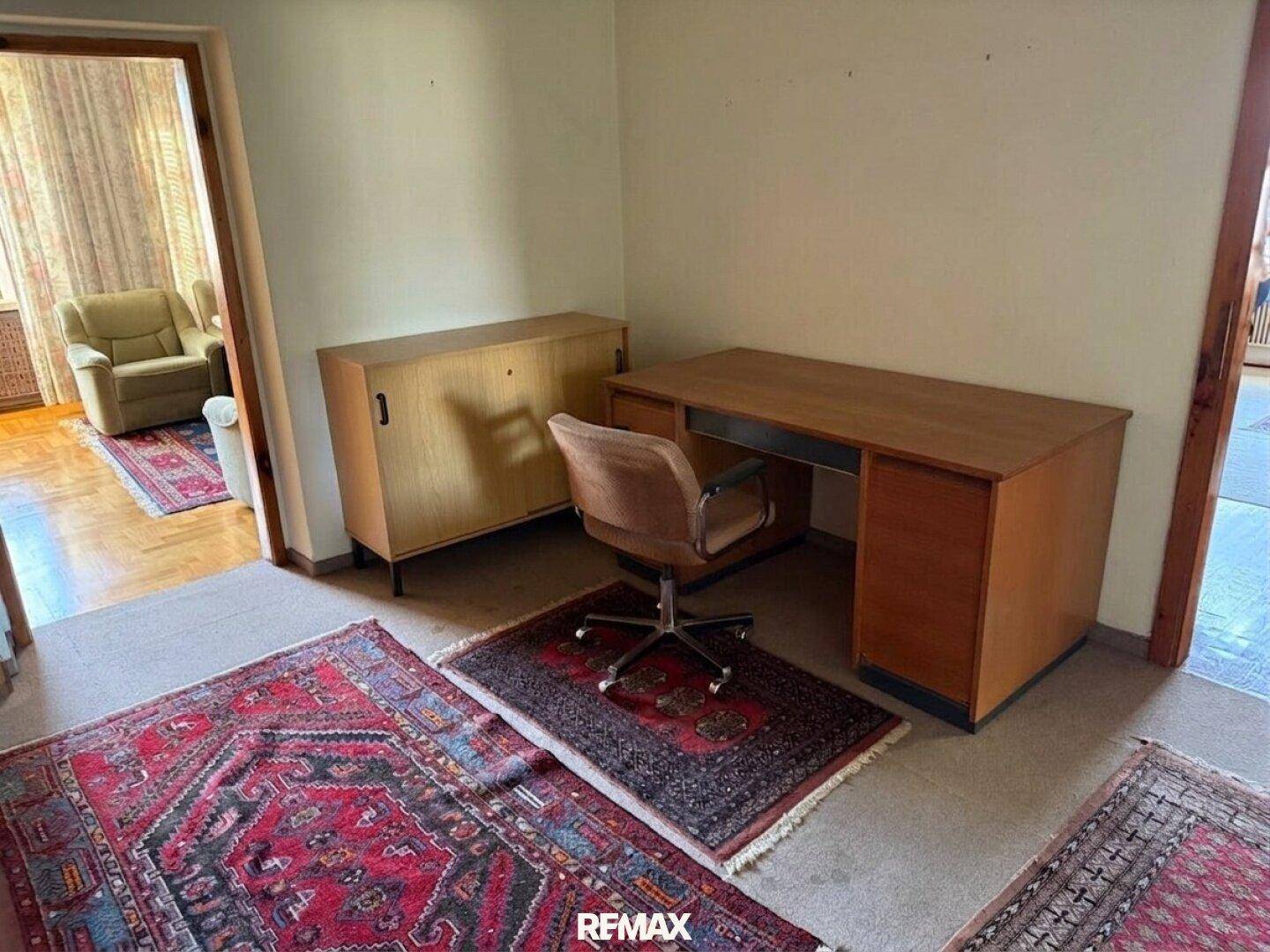 Arbeitszimmer mit Teppichboden, Schreibtisch und Blick in den Wohnbereich.