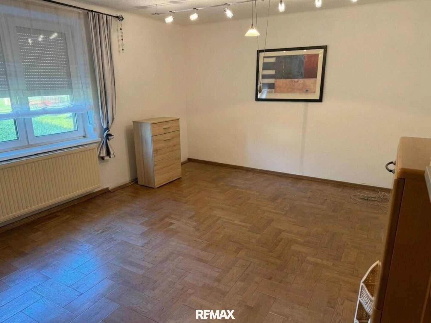 Schlafzimmer mit Fischgrätparkett, Fenster und moderner Beleuchtung.