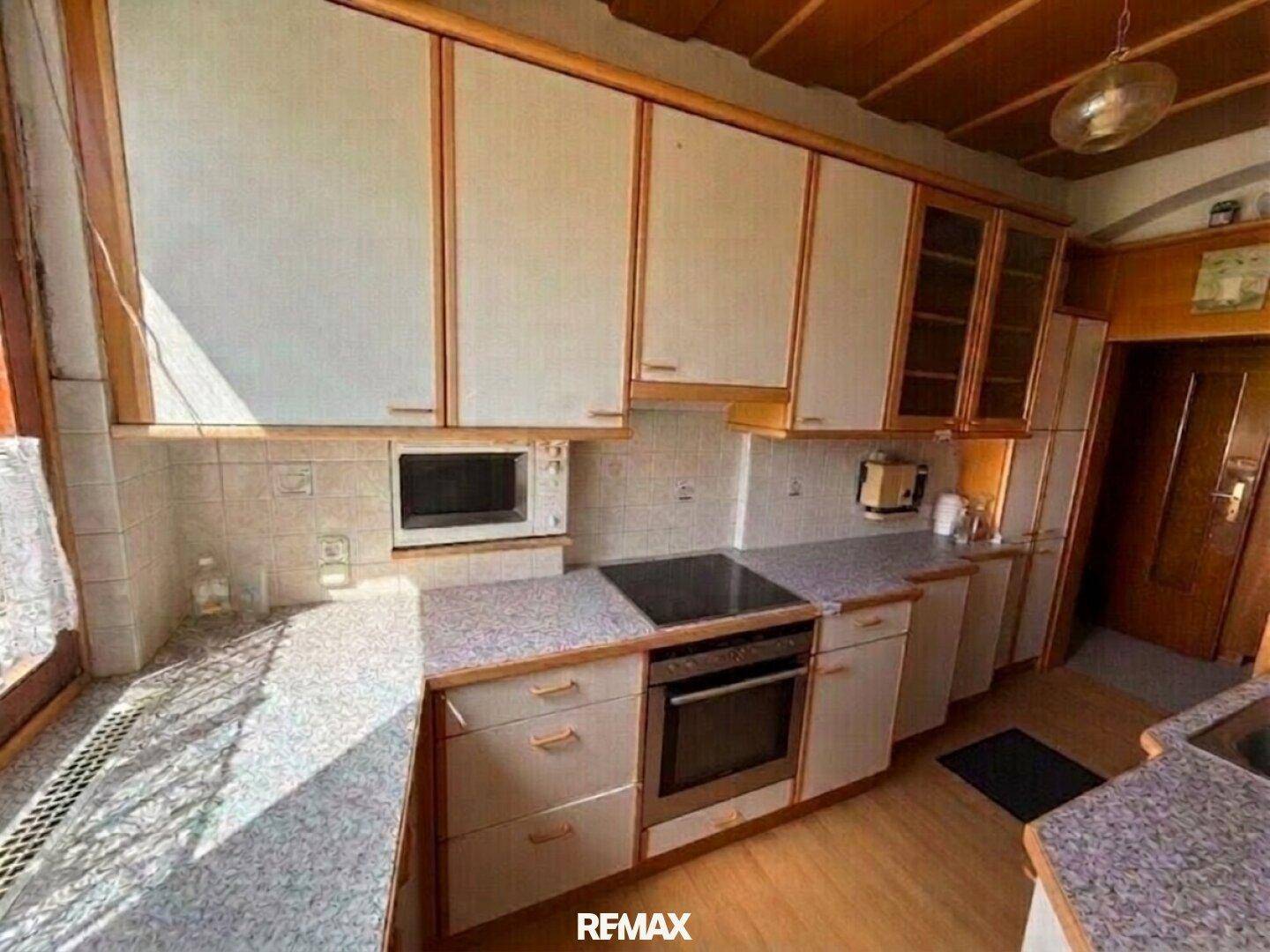 Helle Küche mit Einbauschränken, integriertem Backofen und Mikrowelle, sowie einem Fenster.
