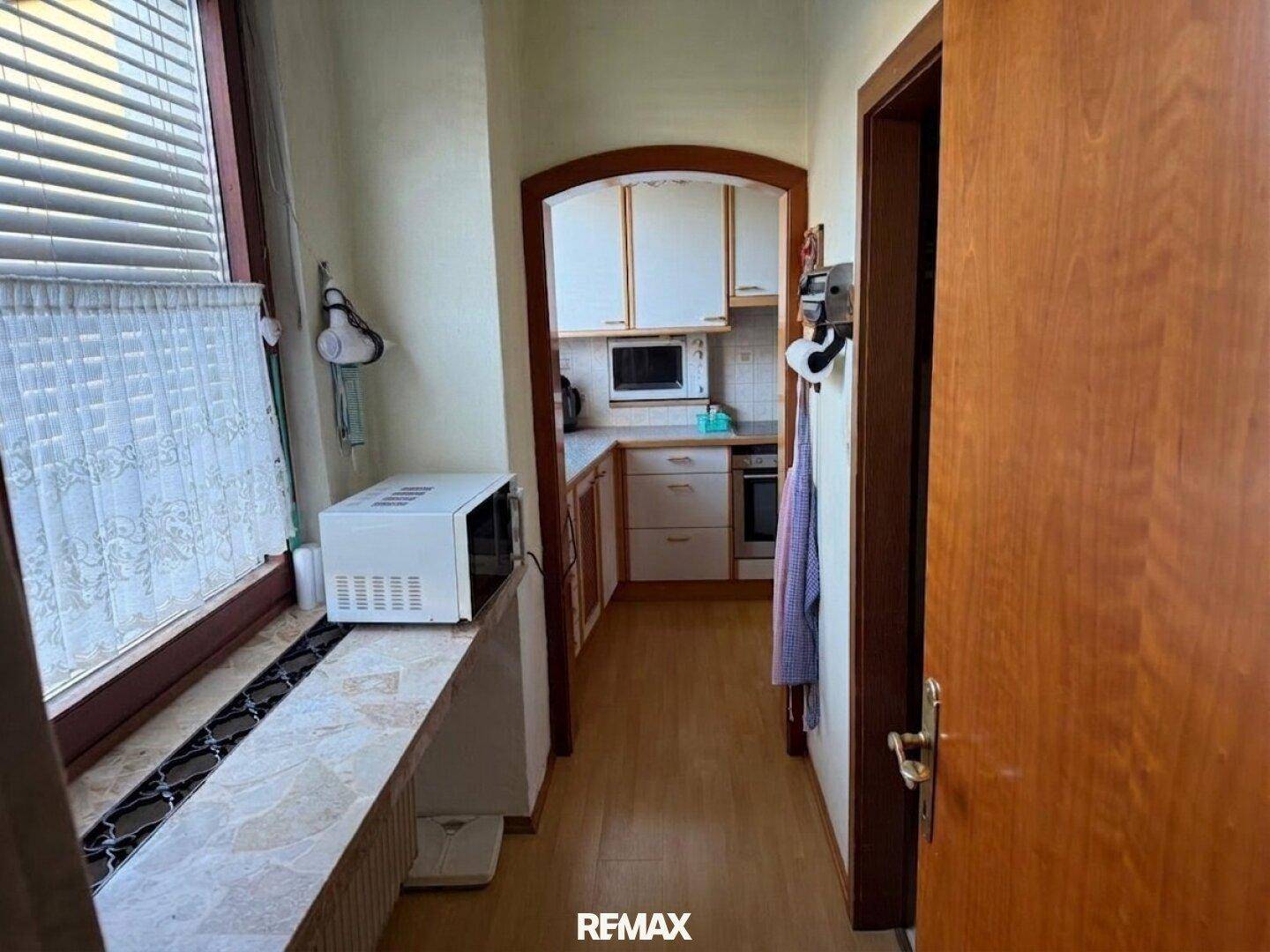 Schmaler Flur mit Fenster, der zu einer funktionalen Küche mit hellen Schränken führt.