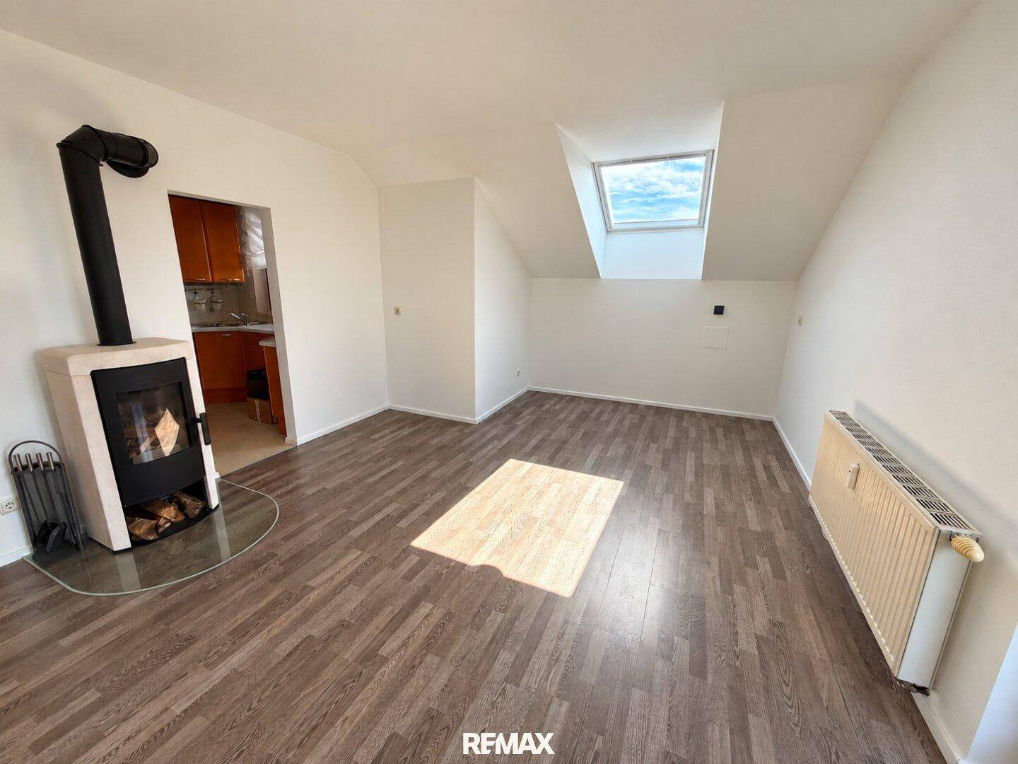 Helles Wohnzimmer mit Holzboden, Kaminofen und Dachfenster, das viel Tageslicht hereinlässt.
