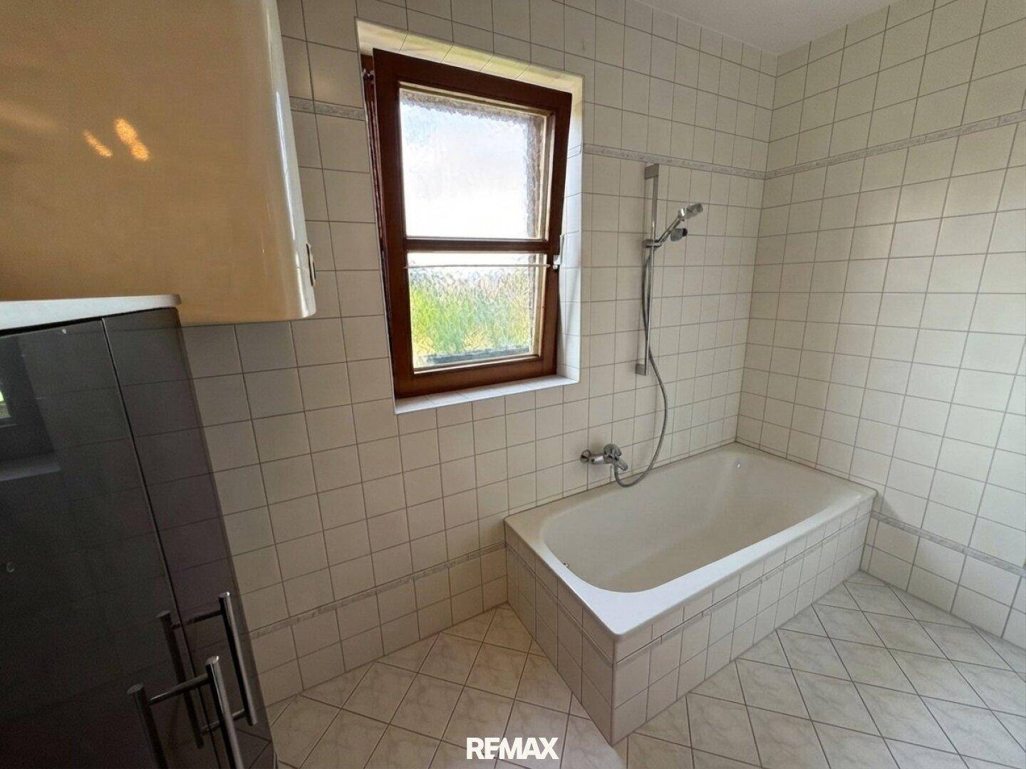 Gefliestes Badezimmer mit Badewanne und Fenster, das für natürliche Belüftung sorgt.