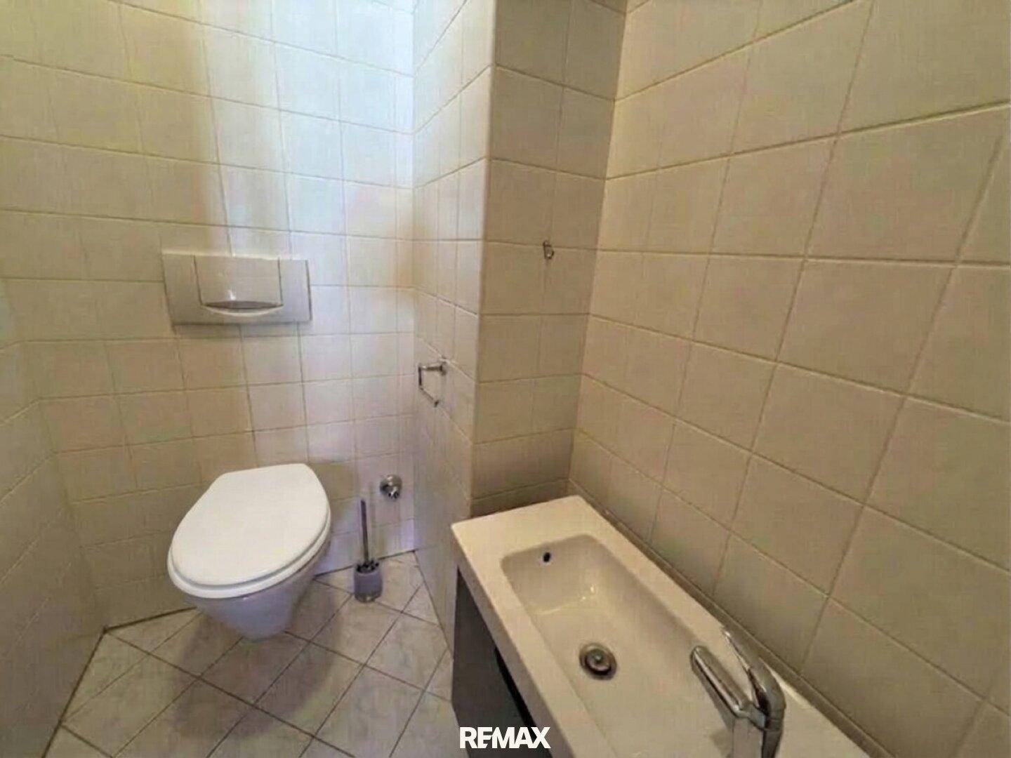 Separates WC mit Wand-WC und kleinem Handwaschbecken, komplett gefliest.