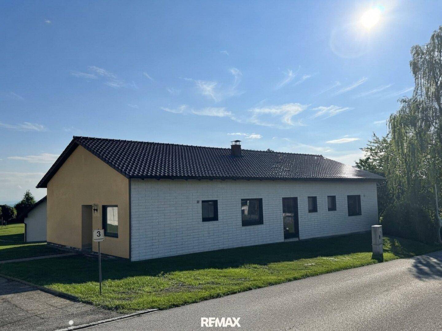 Vorderansicht des Hauses mit weißer Fassade und dunklem Dach unter blauem Himmel.