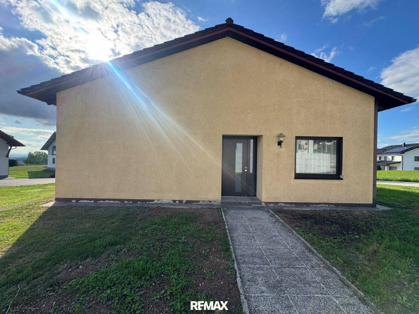 Eingangsbereich des Hauses mit gelber Fassade, dunkler Tür und kleinem Fenster.