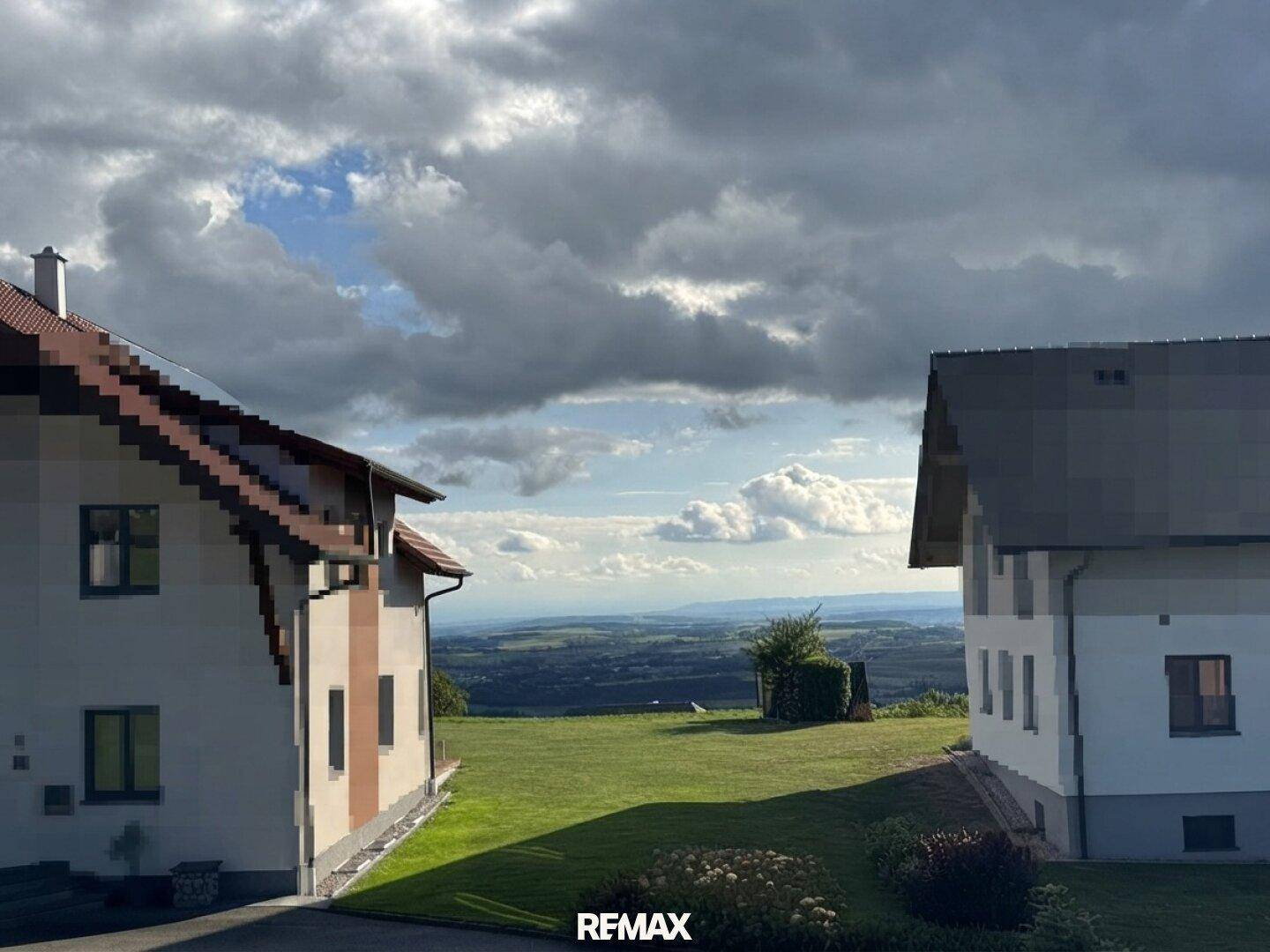 Panoramablick auf die weite Landschaft zwischen zwei Häusern unter bewölktem Himmel.