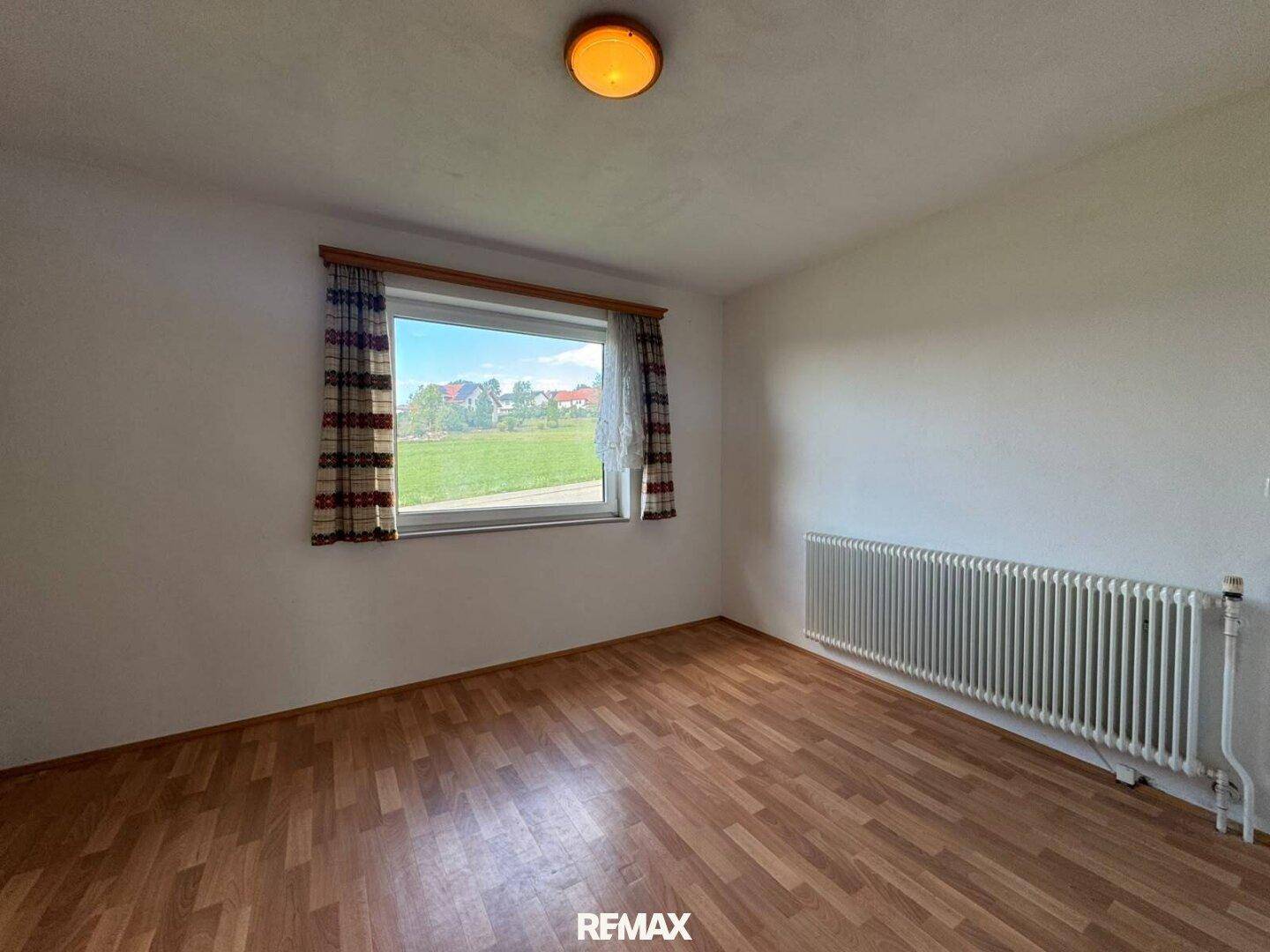 Schlafzimmer mit Laminatboden, weißen Wänden und Fenster mit Blick ins Grüne.