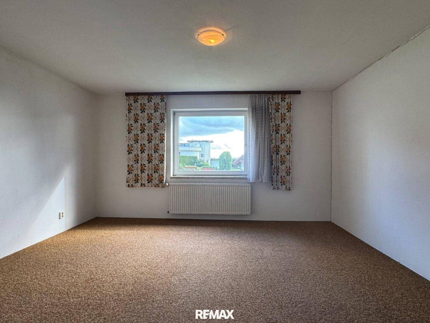 Schlafzimmer mit Teppichboden, weißen Wänden und Fenster mit Blick nach draußen.