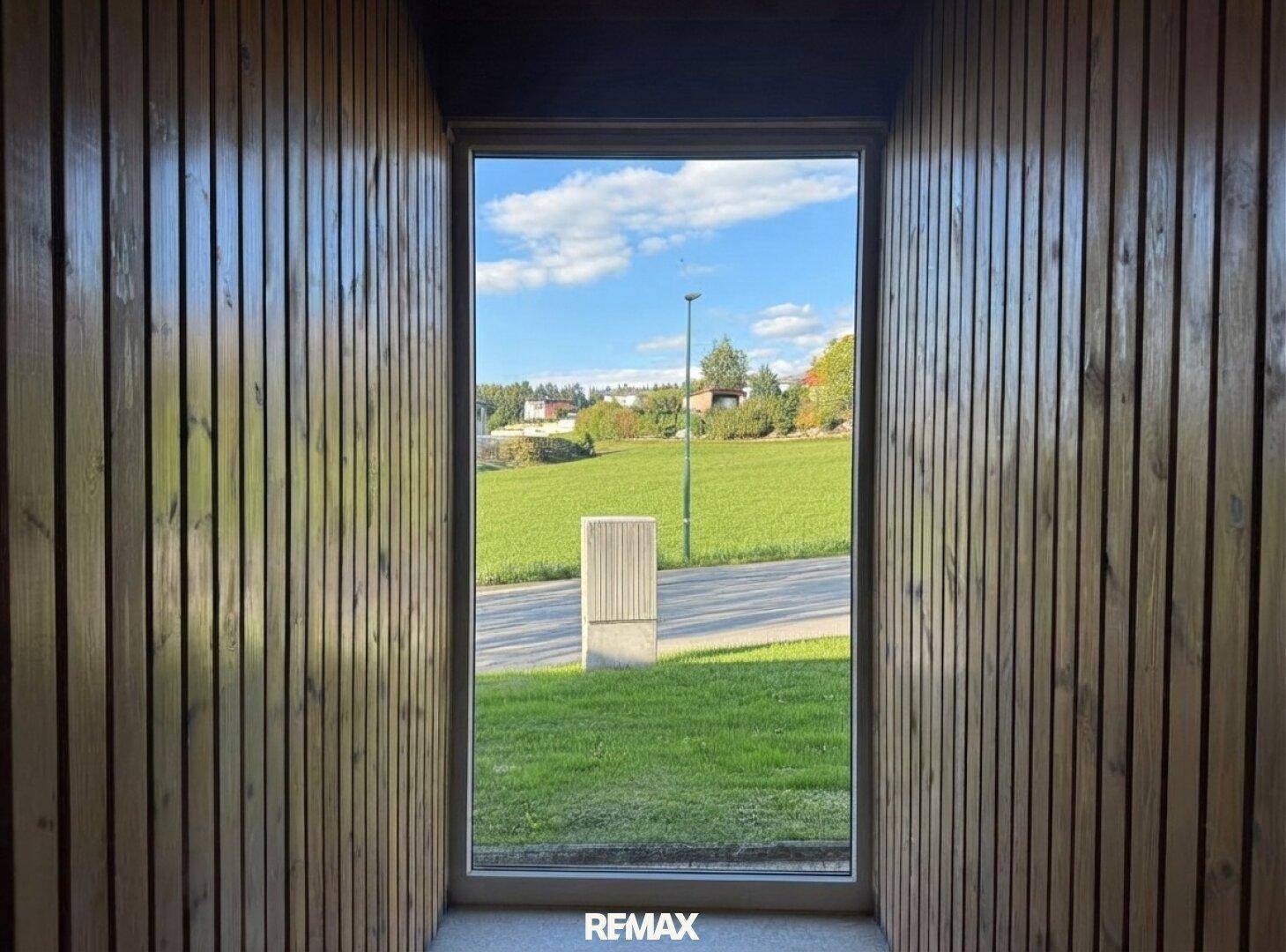 Kleiner Raum mit Holzvertäfelung und Fenster mit Blick auf die Straße und Wiese.