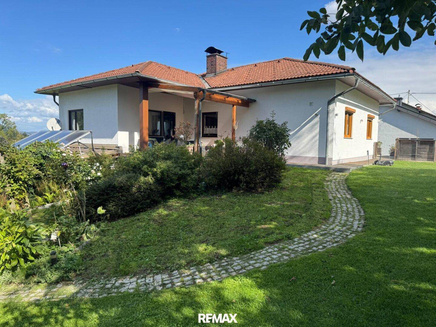 Seitlicher Blick auf das Haus mit gepflegtem Garten, Steinweg und überdachtem Terrassenbereich.