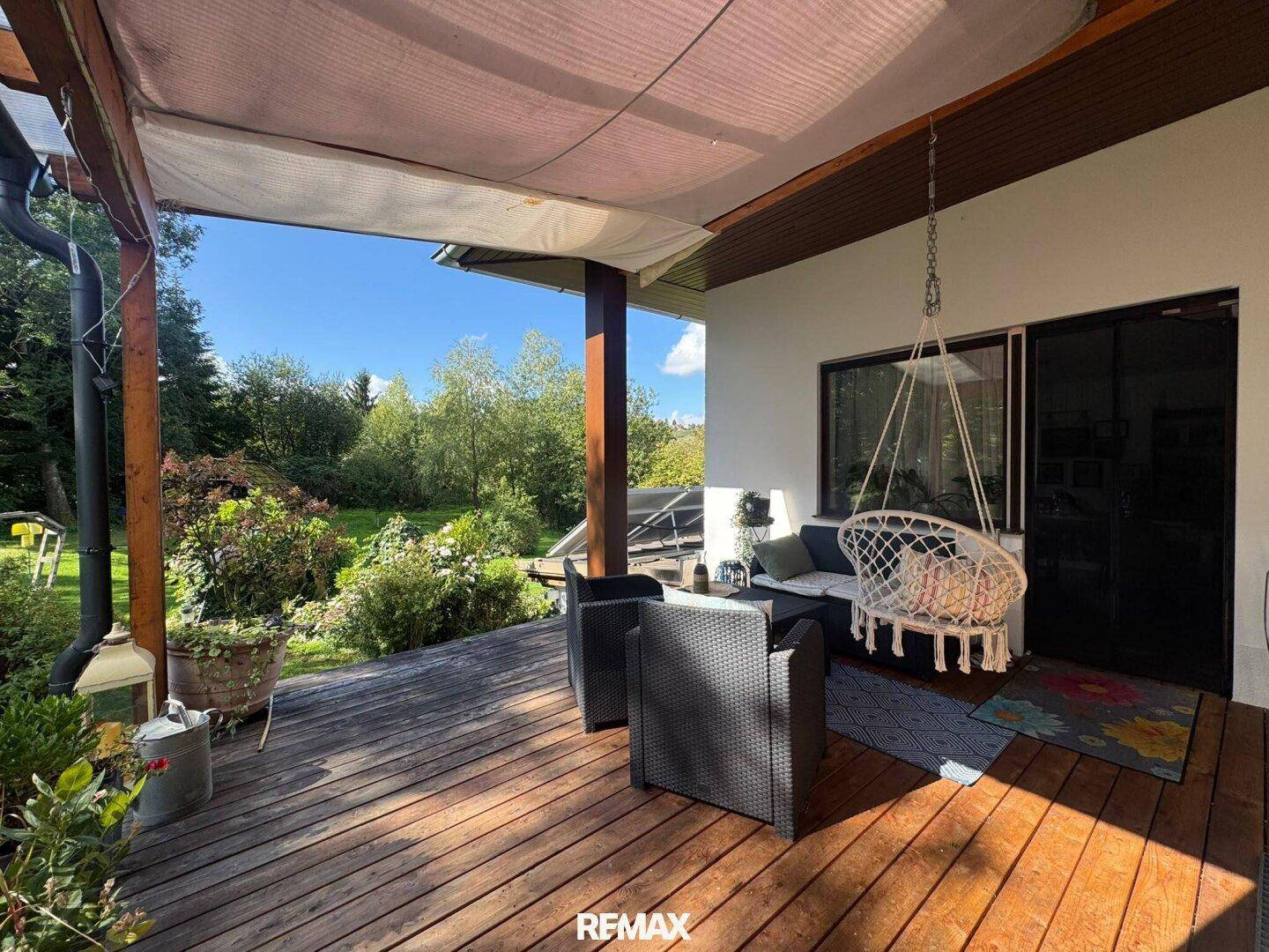 Gemütliche überdachte Terrasse mit Holzboden, Sitzgelegenheiten und Blick ins Grüne.