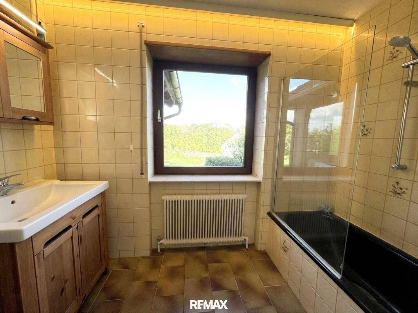 Helles Badezimmer mit Duschbereich, Holzwaschtisch und Fenster mit Blick ins Grüne.