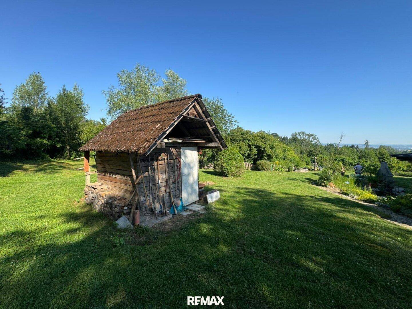 Rustikales Gartenhaus aus Holz mit Ziegeldach, umgeben von Rasen und Bäumen.