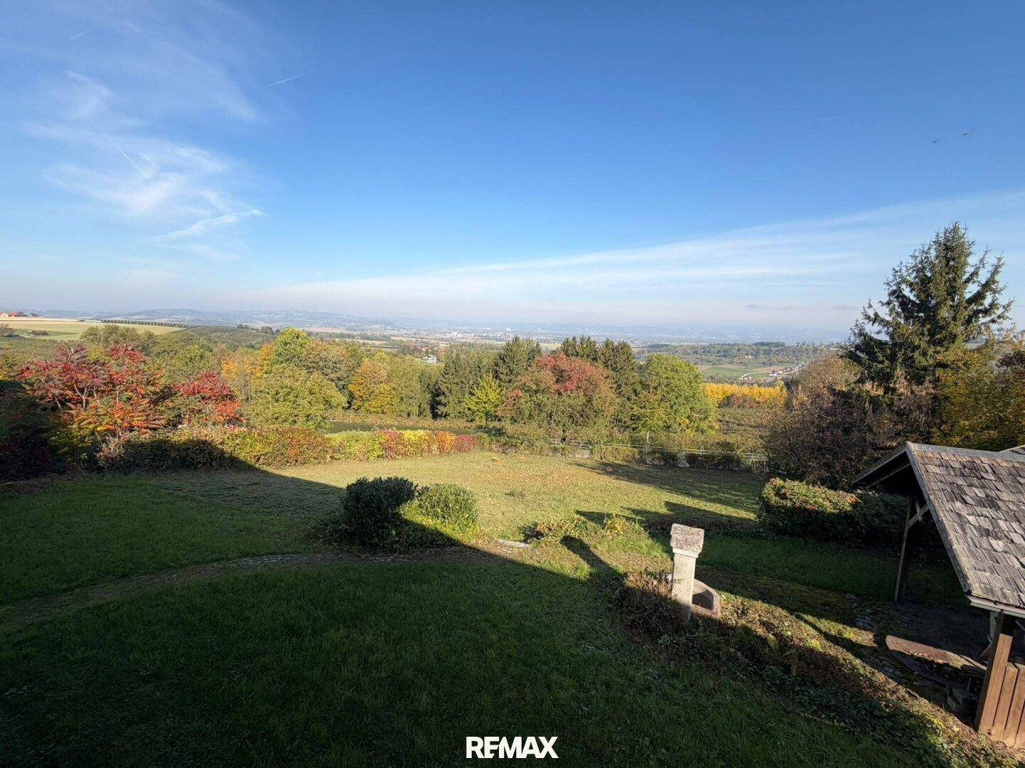 Weitläufiger Gartenbereich mit Fernblick über die Landschaft und grüne Hügel unter blauem Himmel.