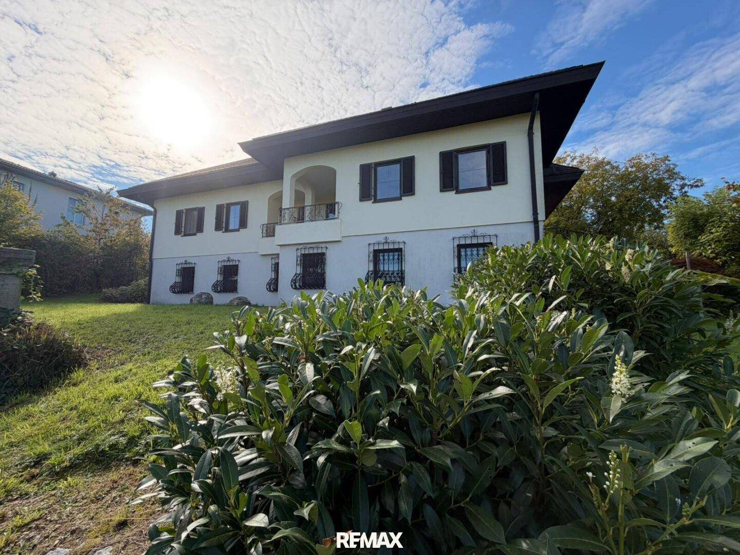 Ansicht des Hauses von der Seite, umgeben von üppigem Grün und Sträuchern unter sonnigem Himmel.