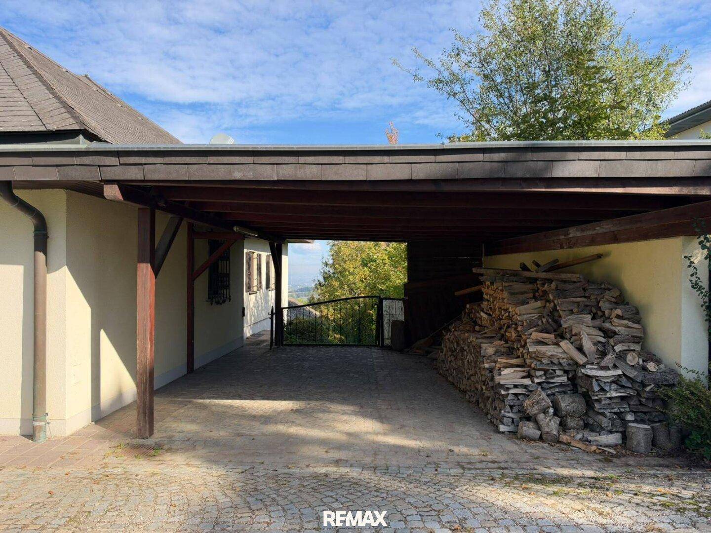 Überdachter Stellplatz oder Carport mit Holzkonstruktion und gestapeltem Brennholz.