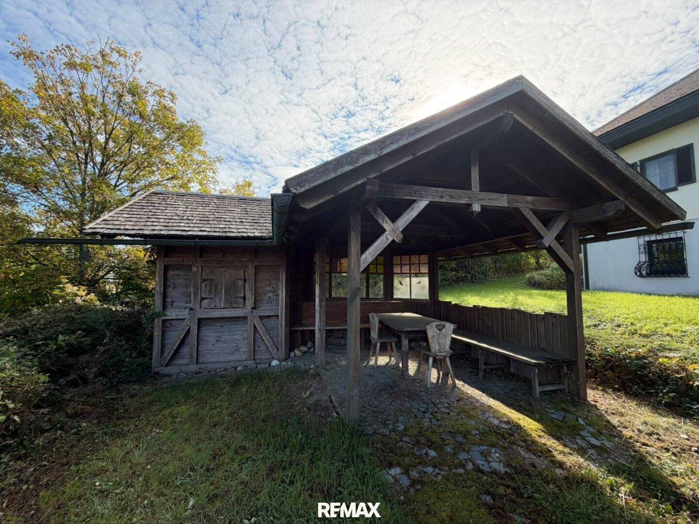 Rustikales Gartenhaus mit überdachtem Sitzbereich und Holztisch, ideal für gesellige Stunden.