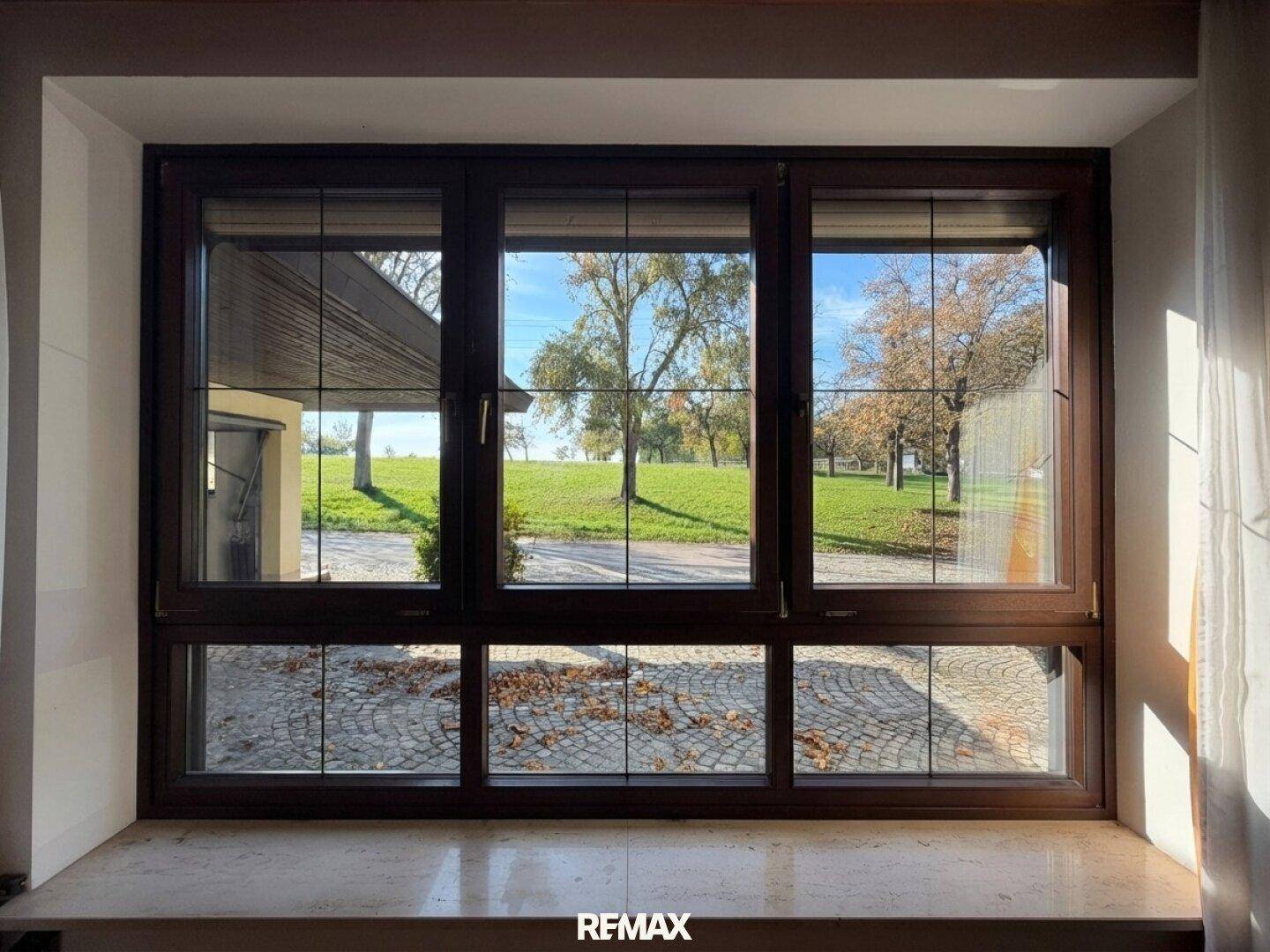 Großes Fenster mit Blick auf den gepflasterten Hof und die grüne Umgebung.
