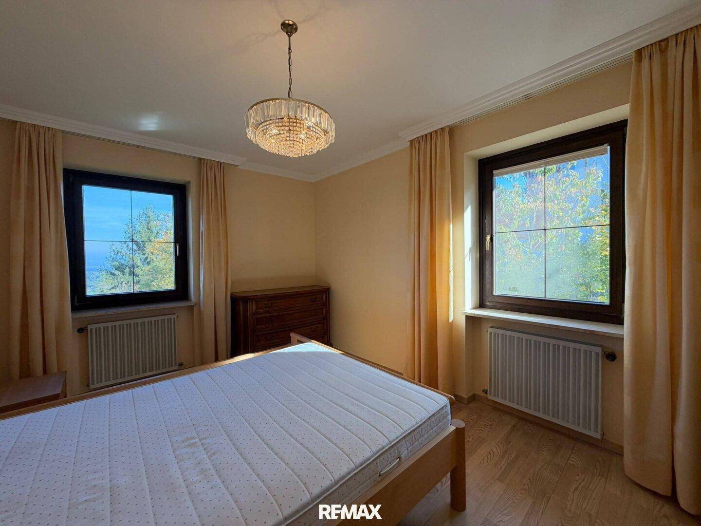 Helles Schlafzimmer mit Holzfußboden, Doppelbett und zwei Fenstern für viel Tageslicht.