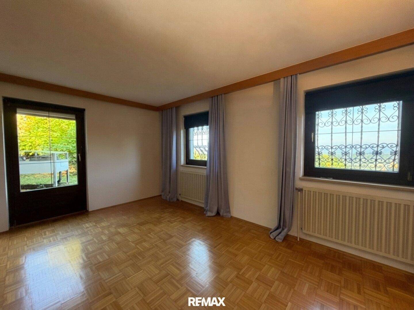Heller Raum mit Parkettboden, Fenster mit Gitter und Zugang zu einem Außenbereich.