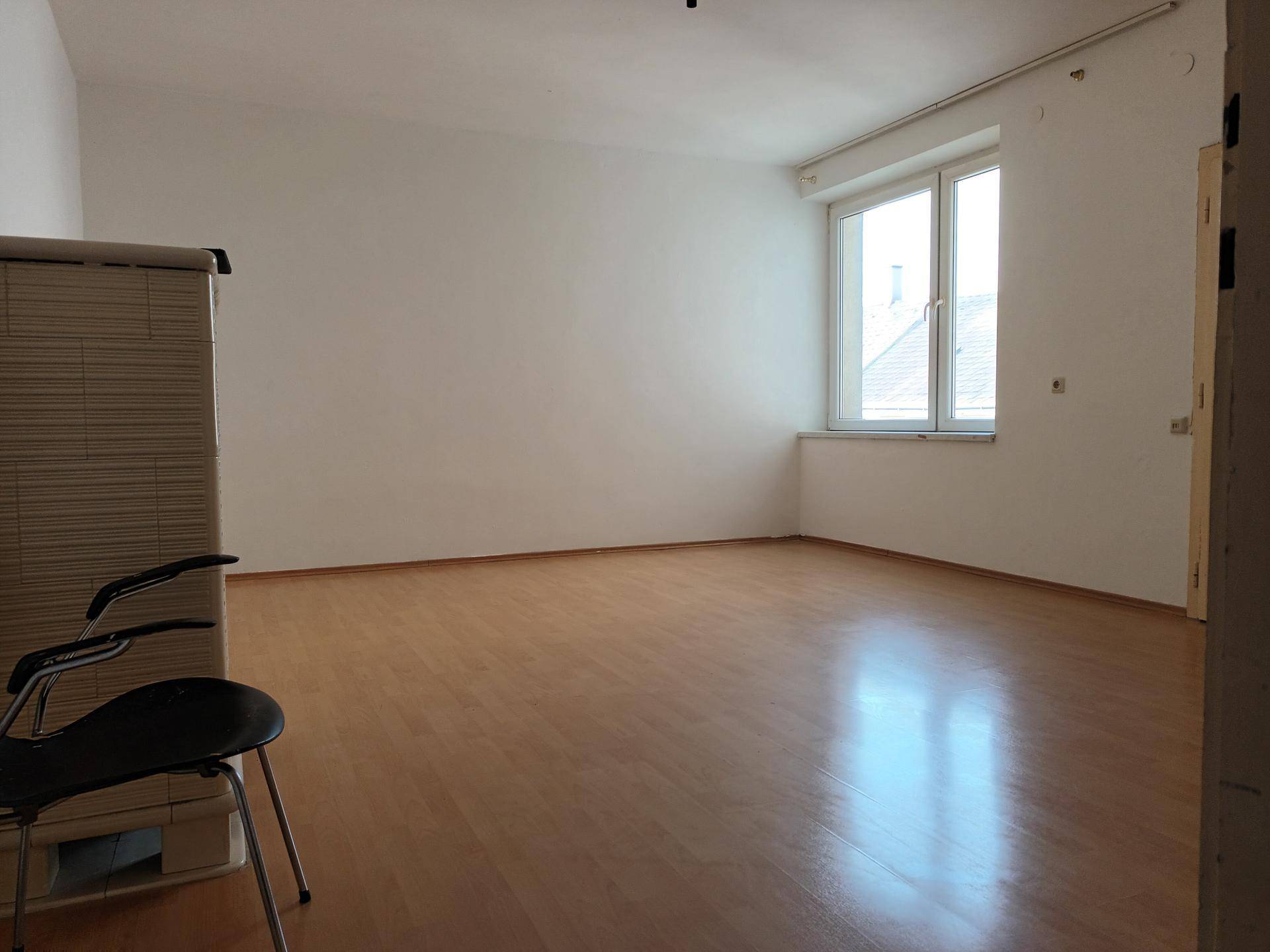 Geräumiger, leerer Raum mit viel Tageslicht durch große Fenster und Laminatboden, hell und offen.
