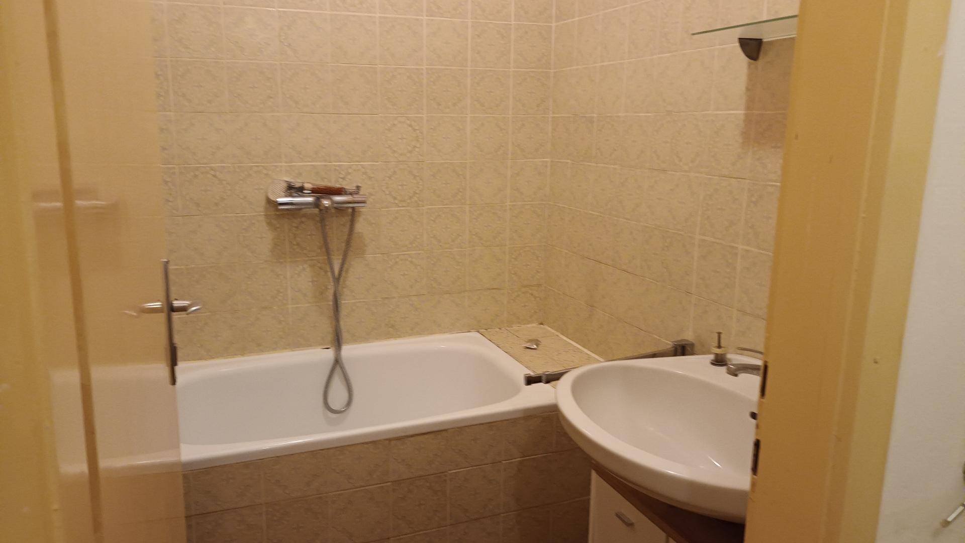 Badezimmer mit Badewanne und Waschbecken, ausgestattet mit hellen Fliesen, funktional und sauber.