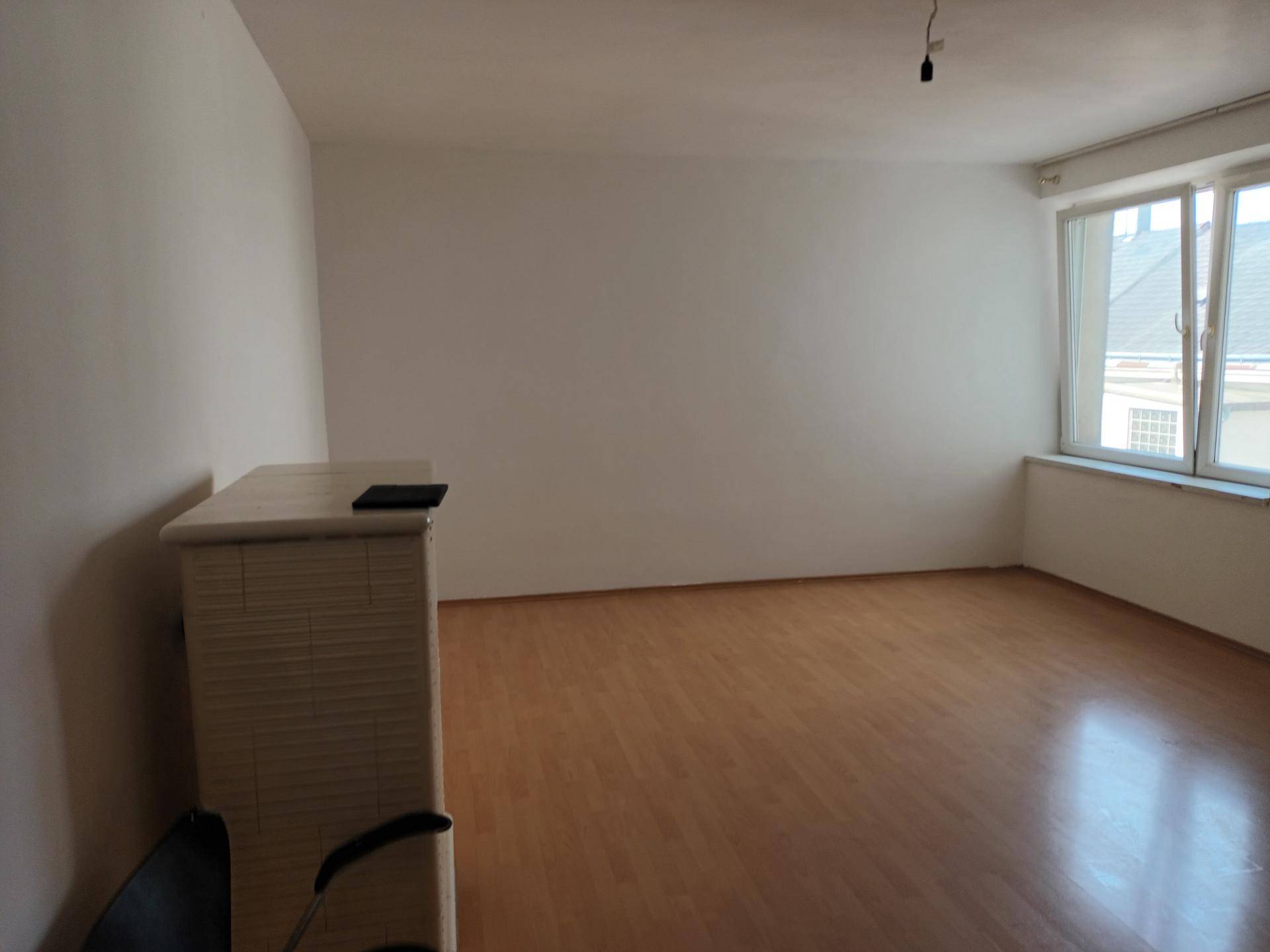 Leerer Raum mit großem Fenster und hellem Laminatboden, bereit zur individuellen Gestaltung.