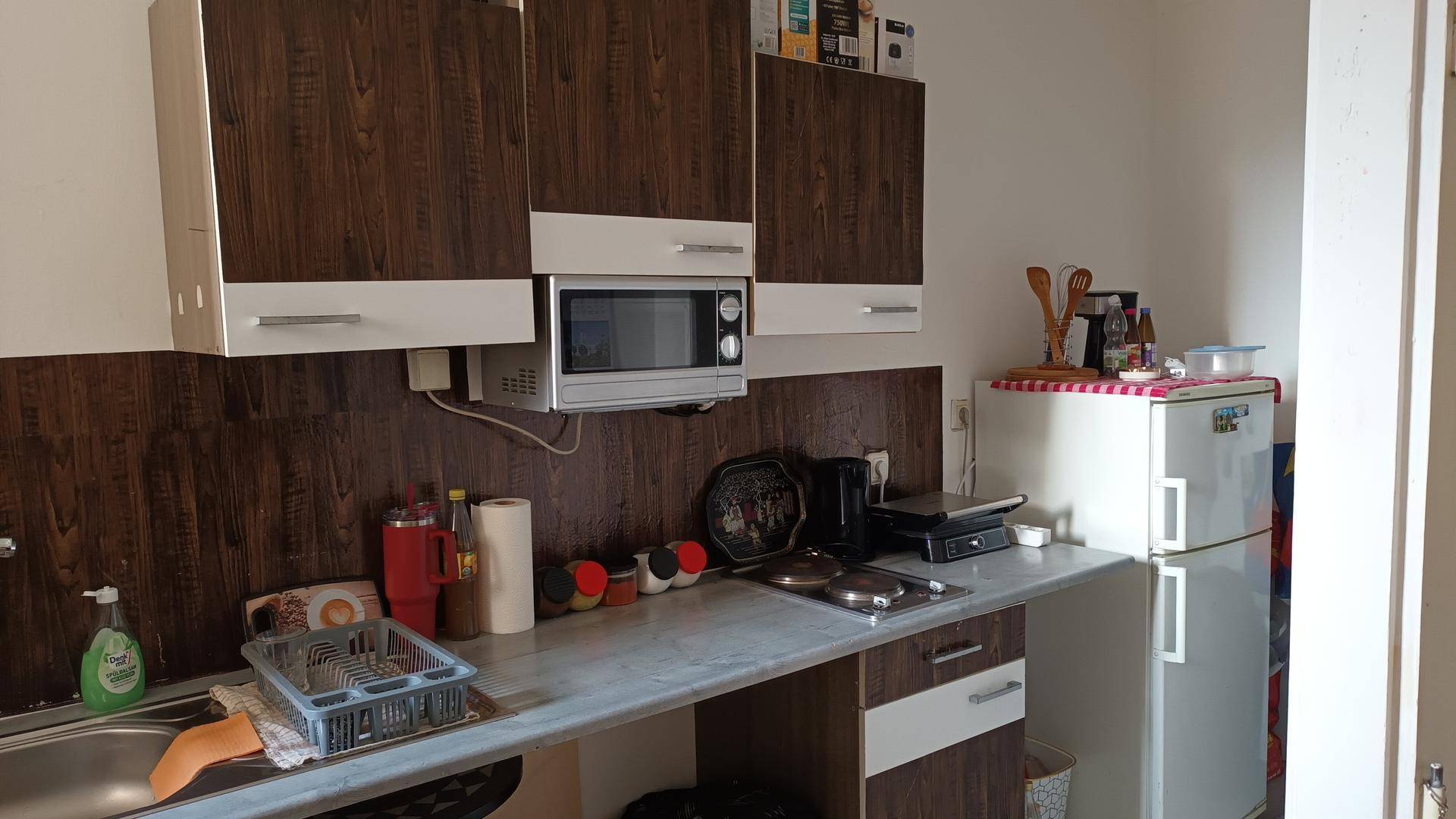 Funktionale Küche mit Holzschränken, Spüle, Mikrowelle und Kühlschrank, praktisch eingerichtet.
