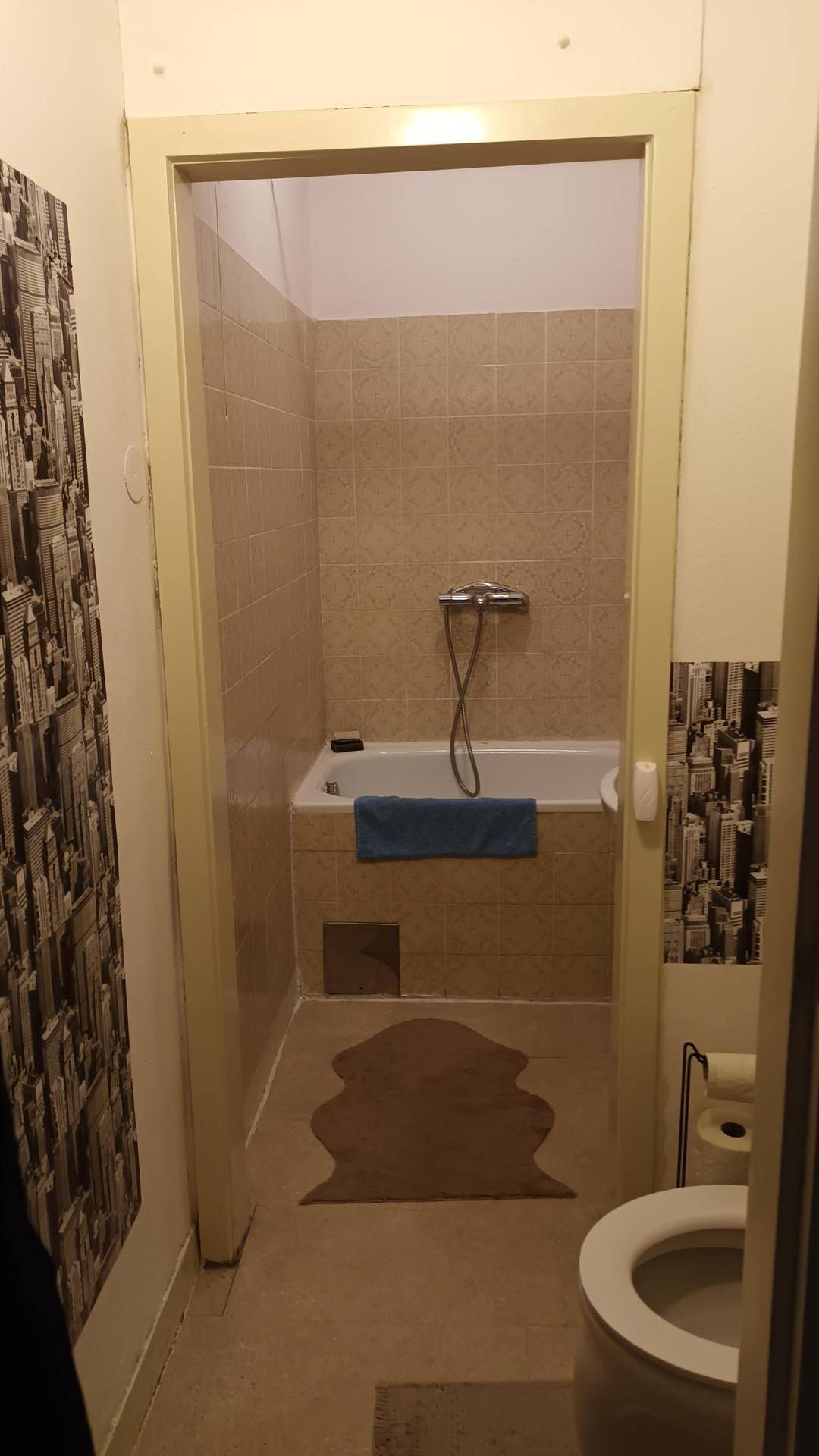 Badezimmer mit Toilette und Blick auf die Badewanne, gefliest in hellem Beige, praktisch eingerichtet.