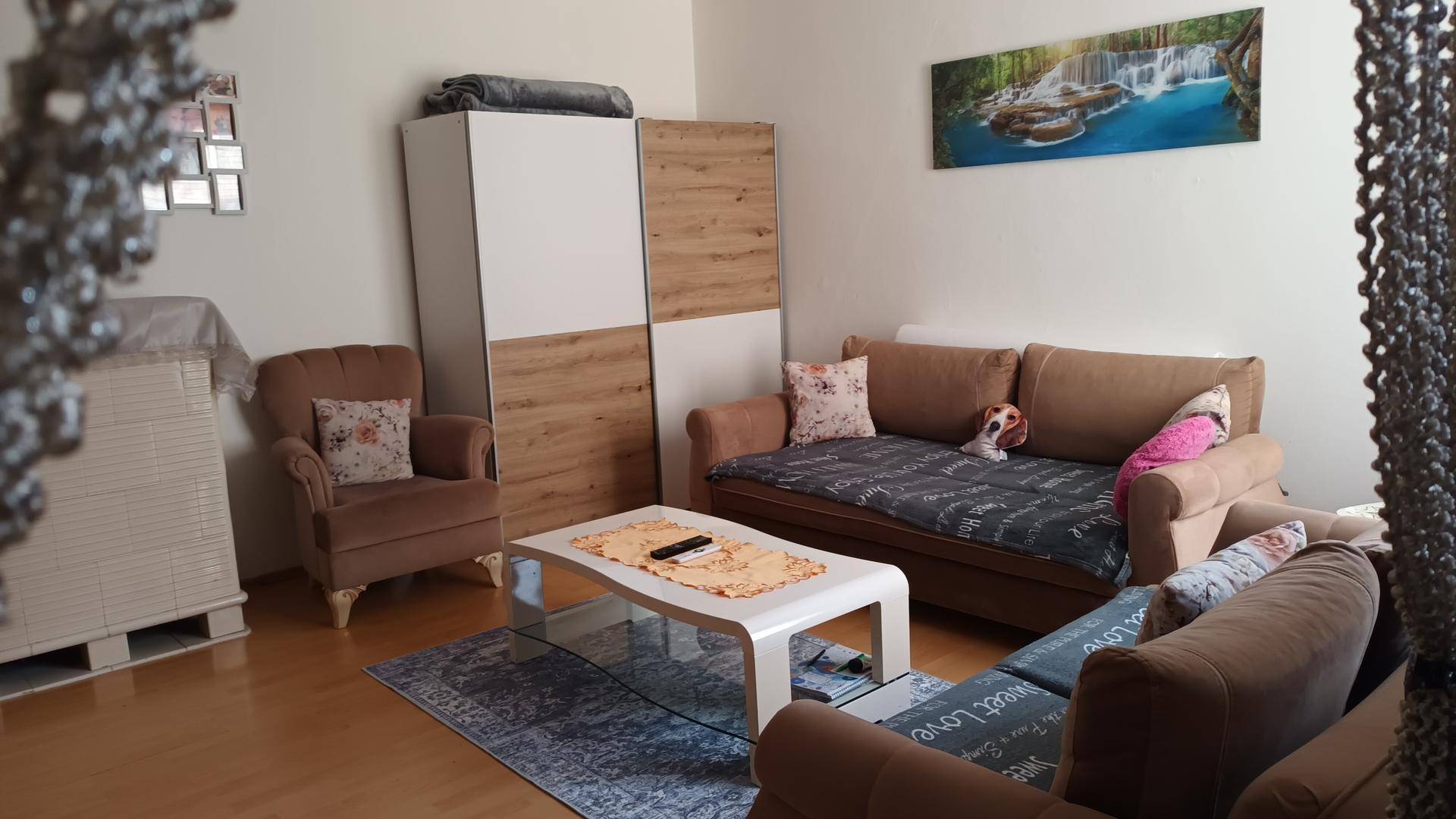 Helles Wohnzimmer mit bequemen Sofas, einem Sessel und einem modernen Kleiderschrank, einladend gestaltet.