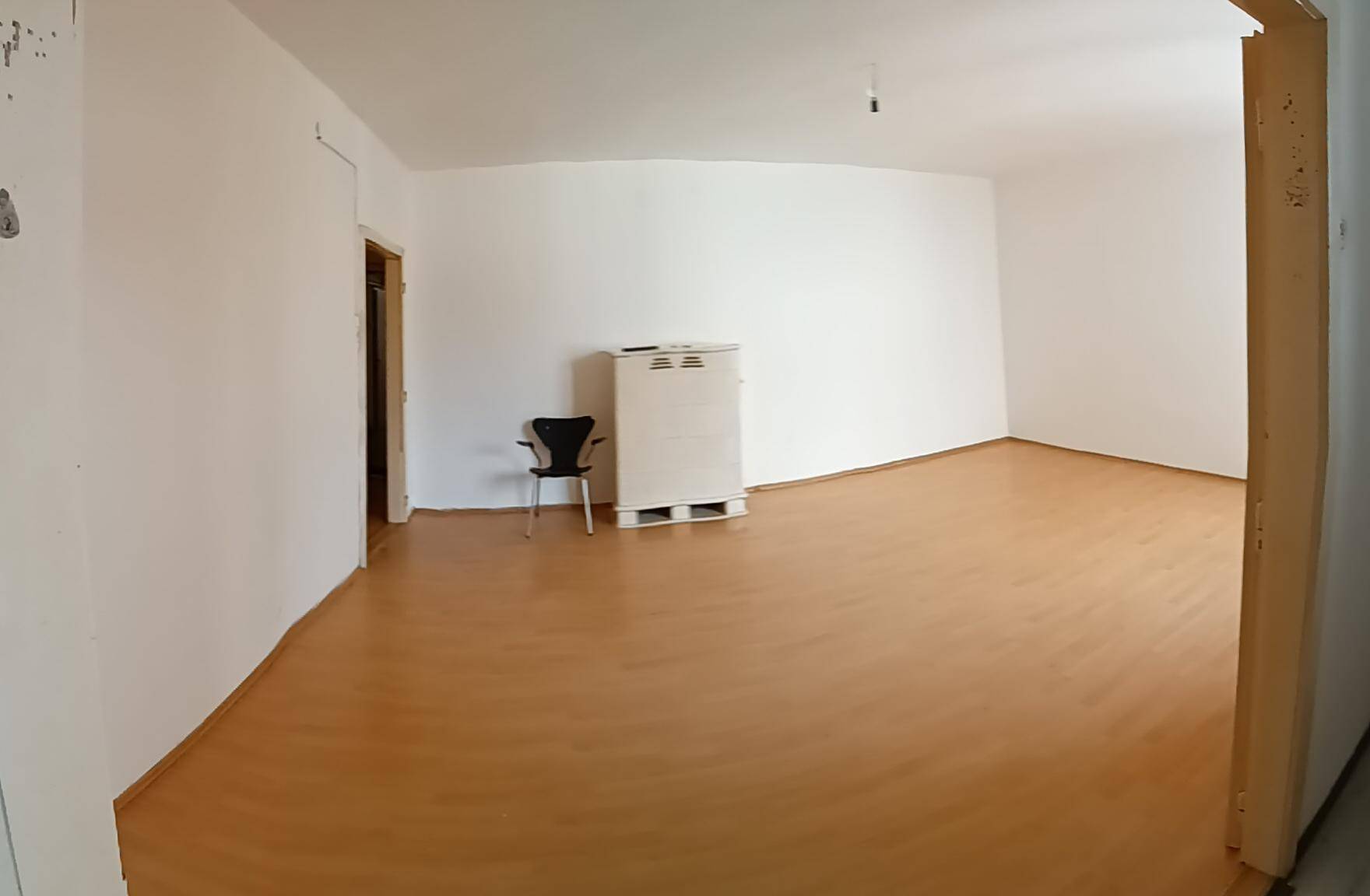 Weitläufiger, leerer Raum mit hellem Laminatboden und einer Tür, vielseitig nutzbar und gepflegt.